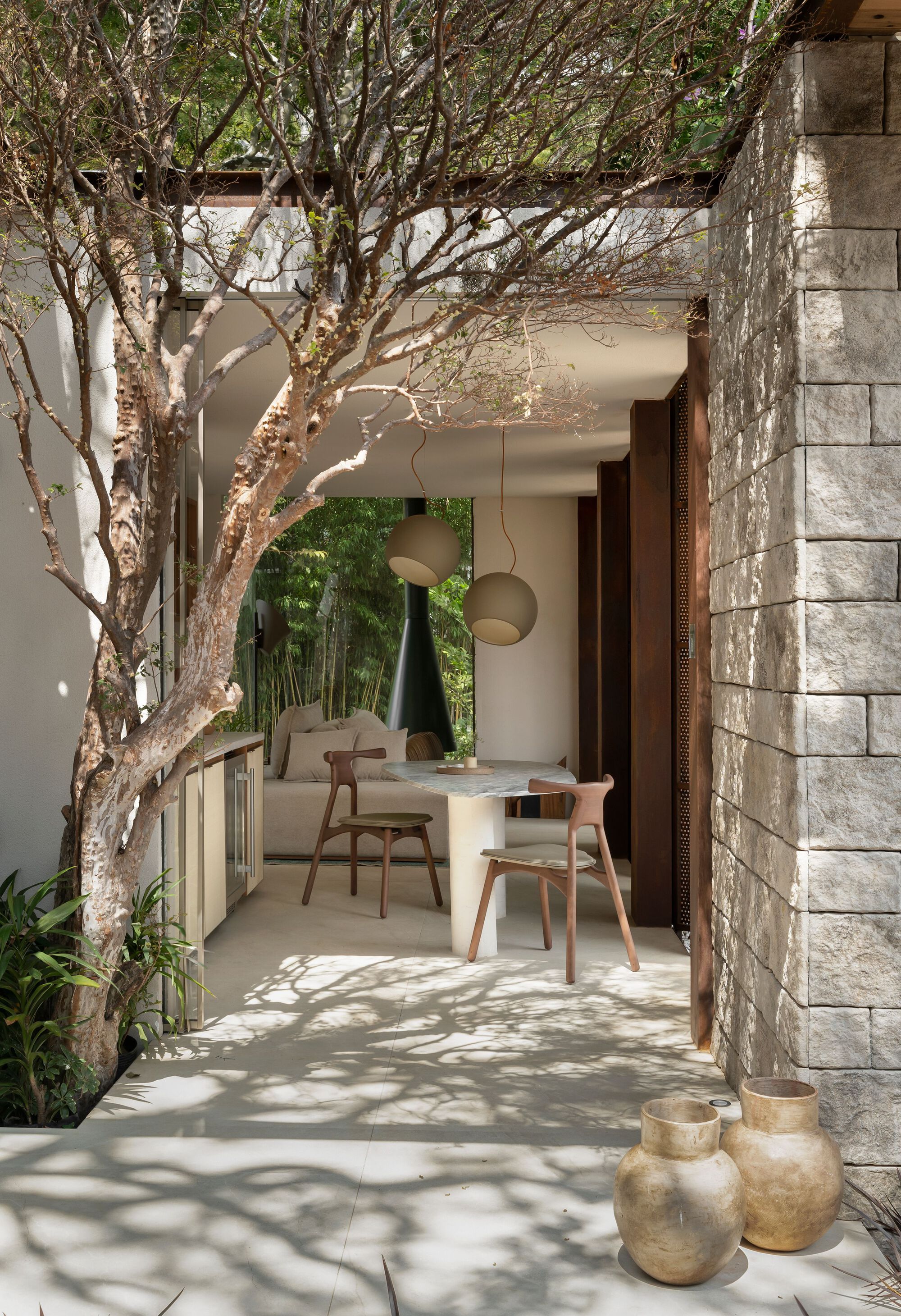 Covered dining terrace framed by concrete block walls with dappled sunlight filtering through overhead branches