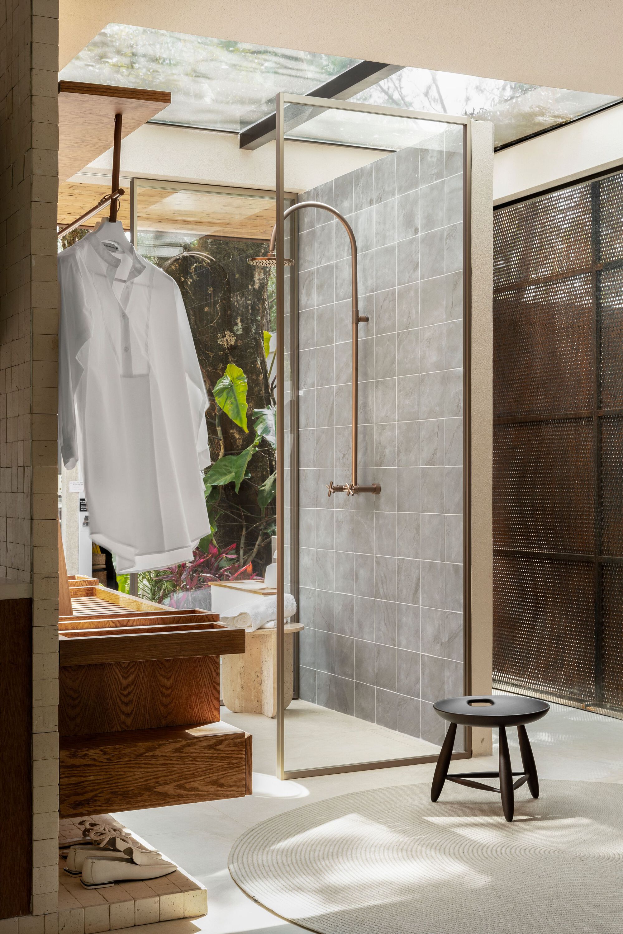 Bathroom with glass-enclosed shower and white tiled wall opening to a planted courtyard