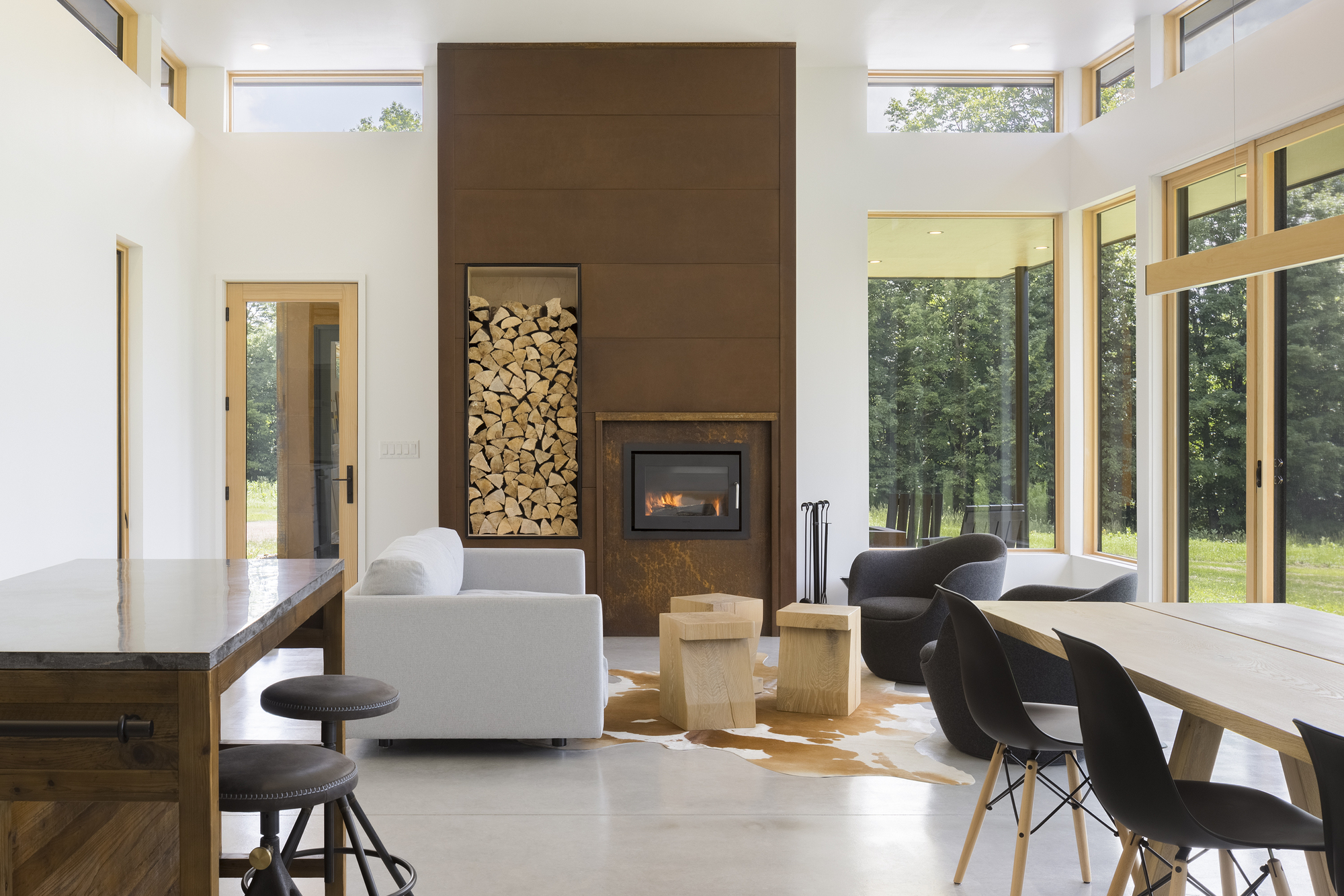 Open living and dining area with double-height fireplace wall containing stacked firewood niche and clerestory windows