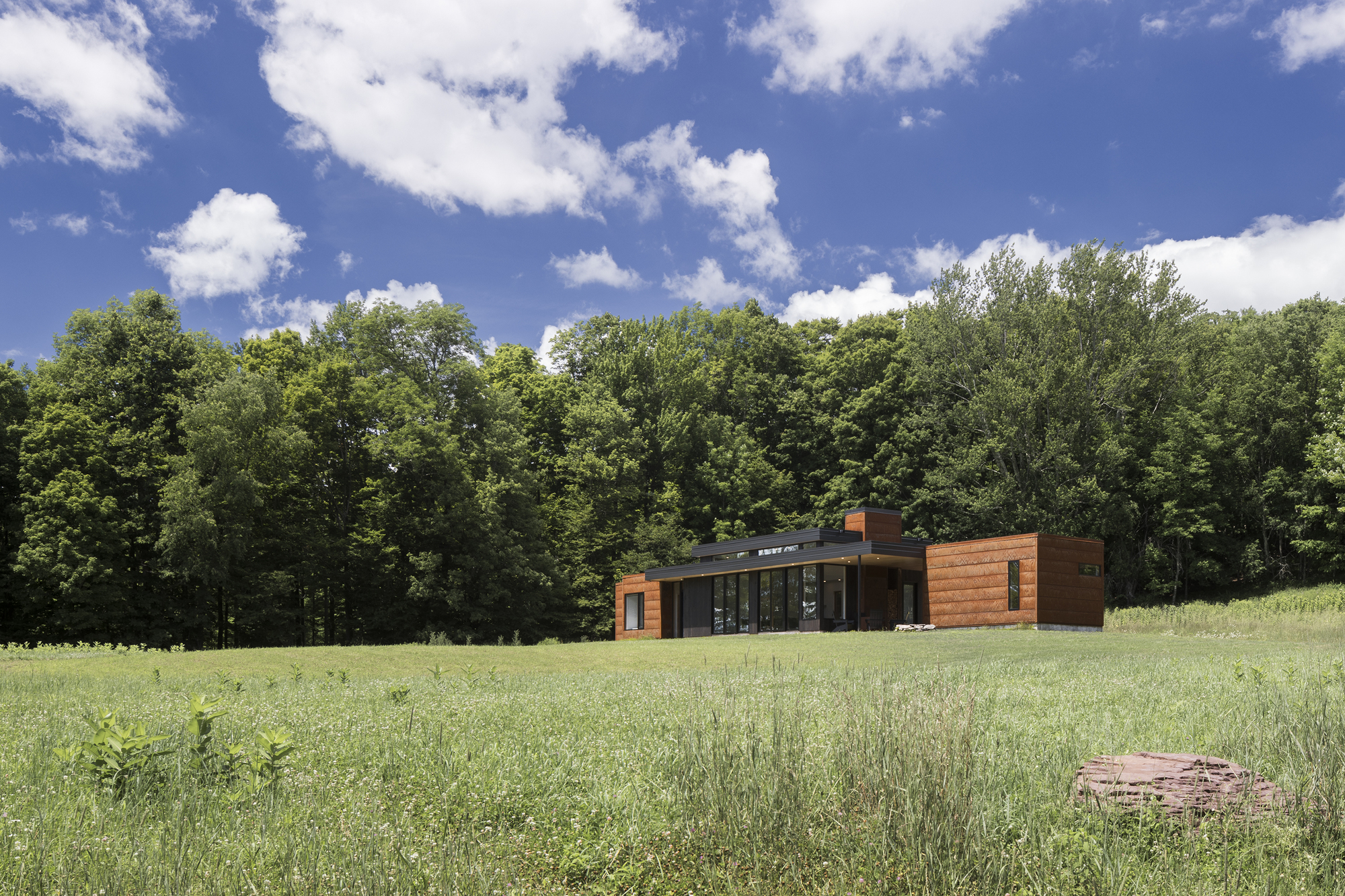Distant view of the horizontal residence with cedar cladding and glazed center volume in a mowed meadow