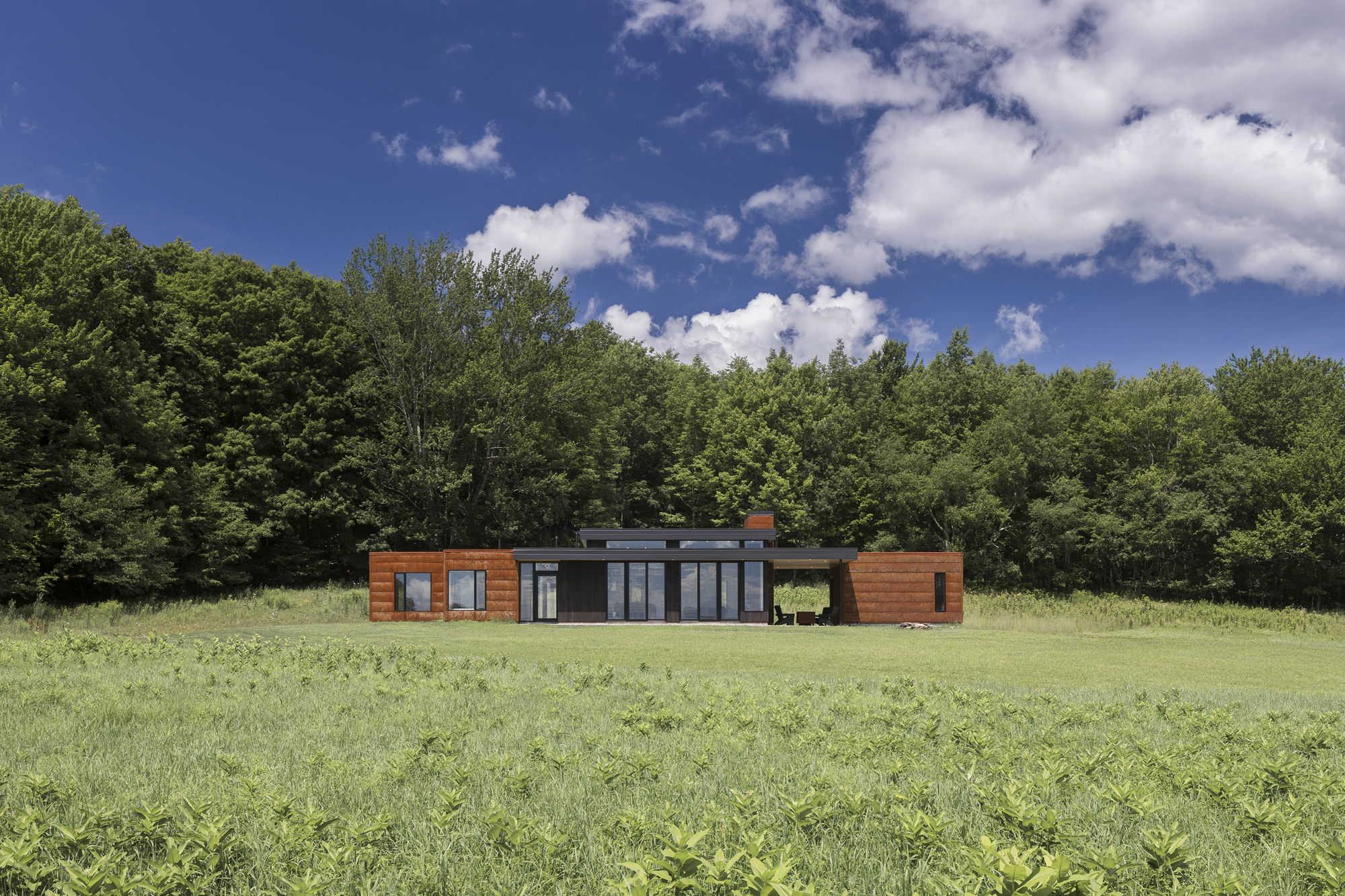 Front facade showing cedar-clad wings flanking a central glazed pavilion under midday sun
