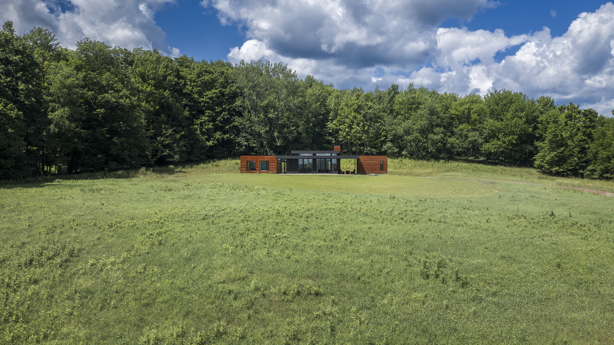 Long view across the sloping meadow with the linear residence anchored against the forest edge