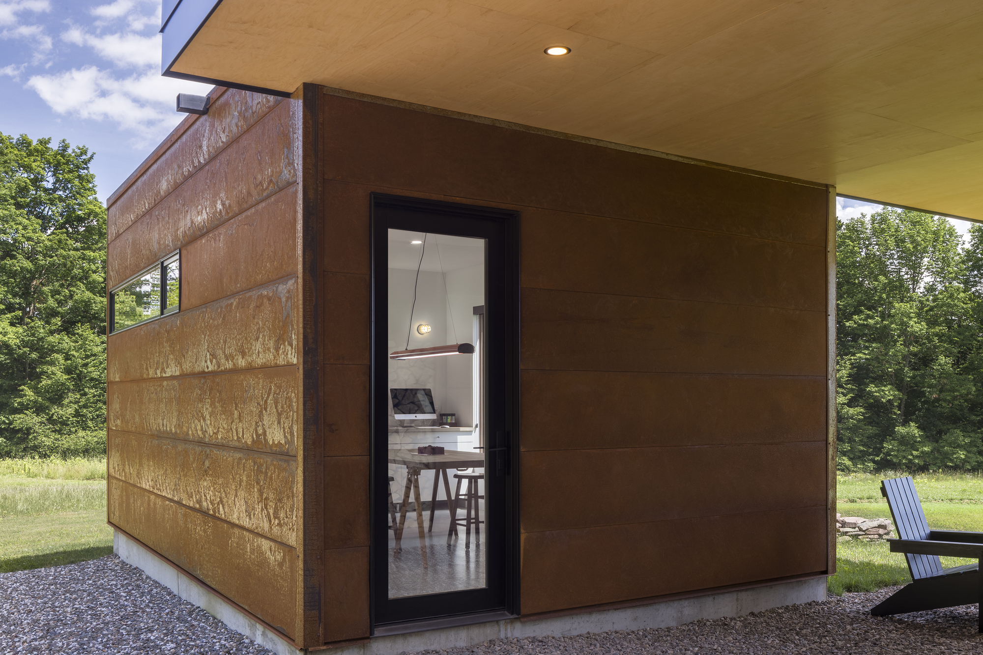 Corner detail of weathered steel panels meeting horizontal cedar siding beneath a deep roof overhang