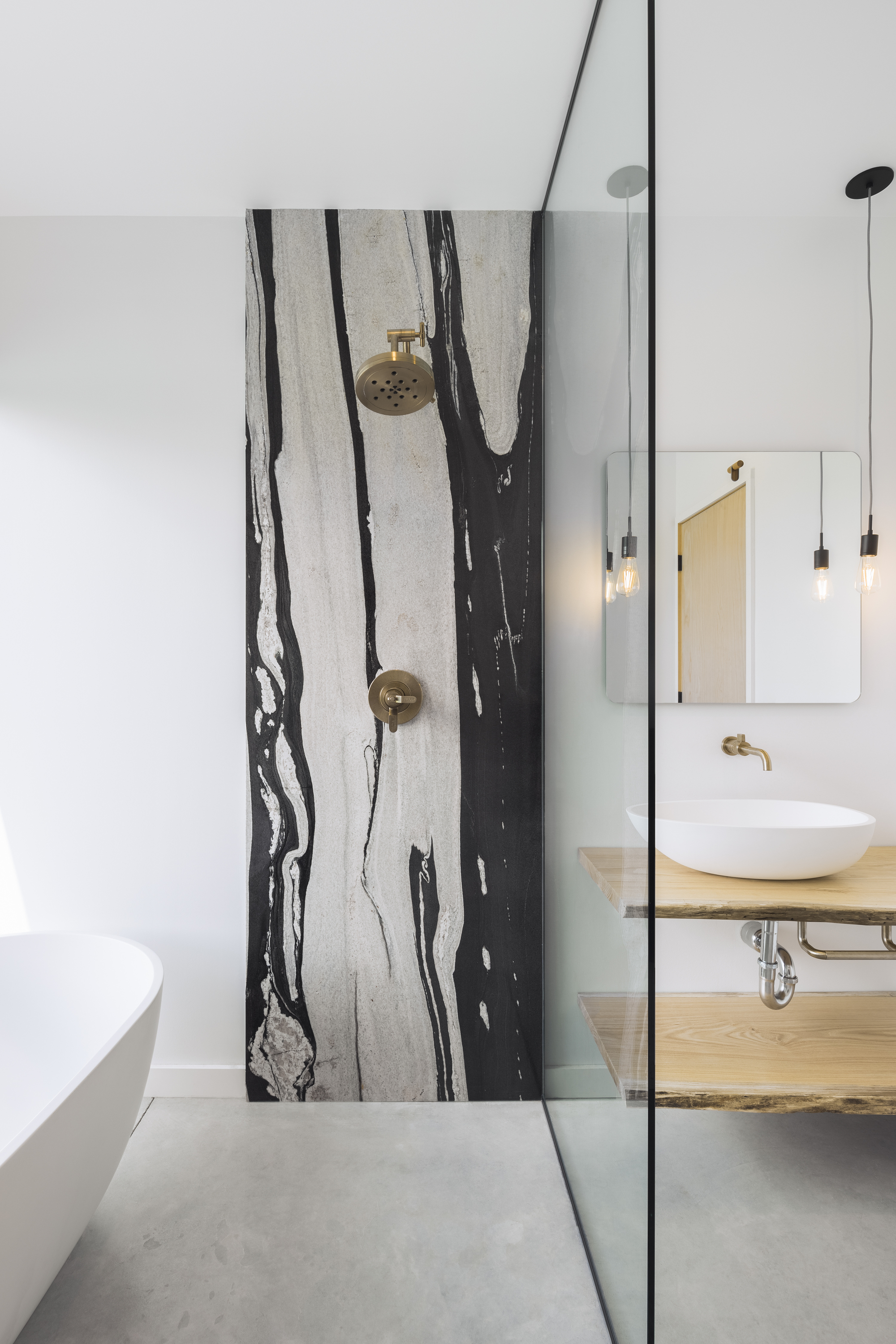 Shower wall clad in black-veined white marble slab with brass fixtures and glass partition