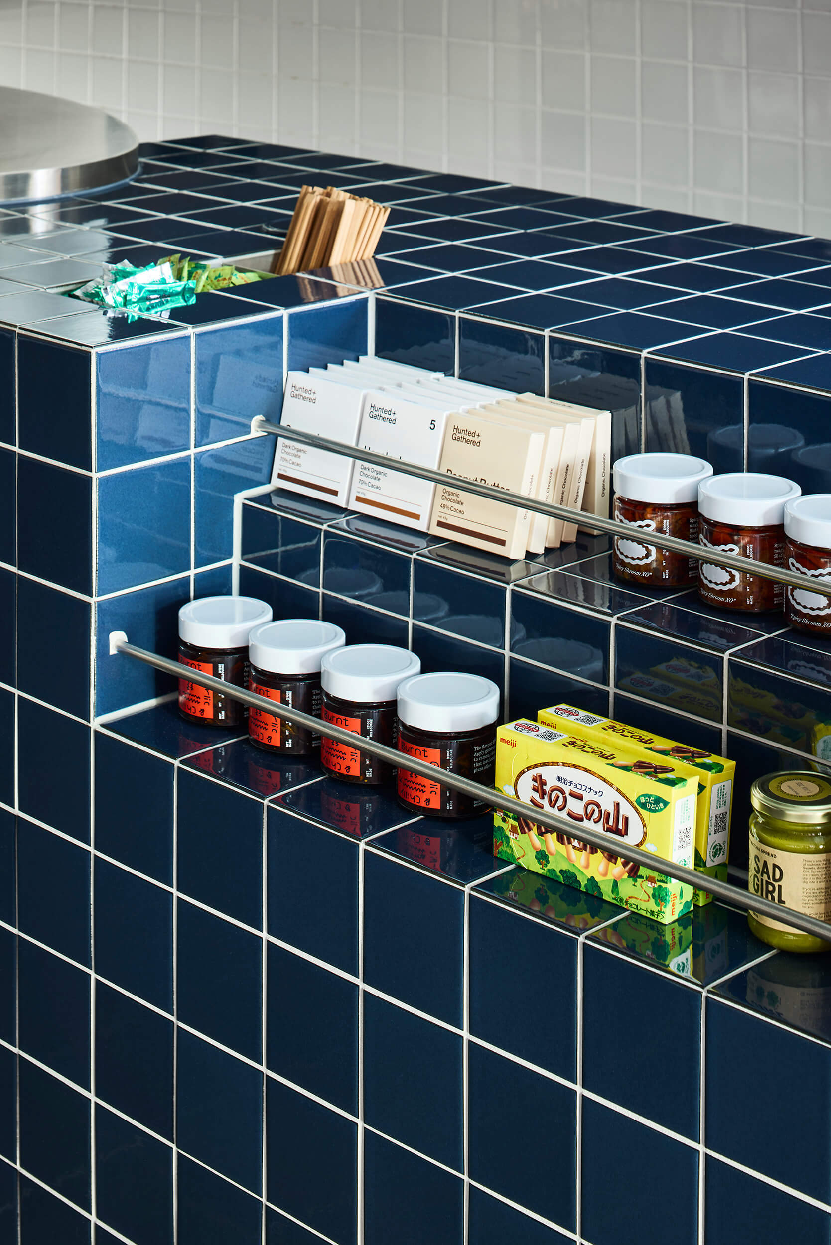 Clear acrylic shelves mounted on blue tile wall holding packaged goods and glass jars with labels