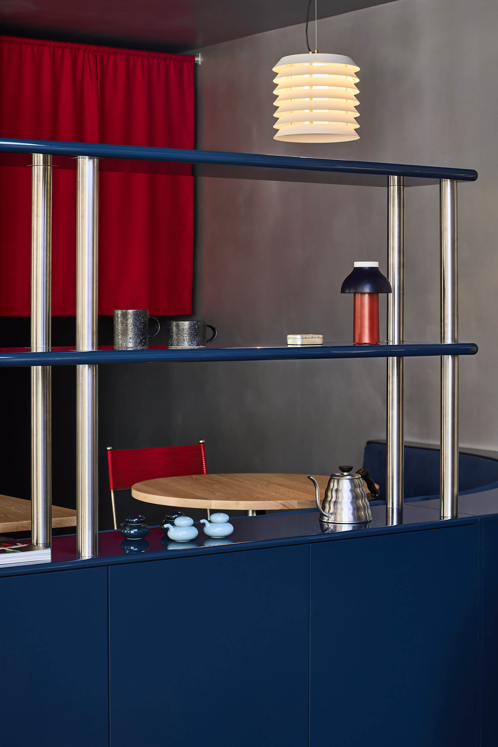 Chrome tube shelving with navy blue surfaces and red curtain behind pendant lamp