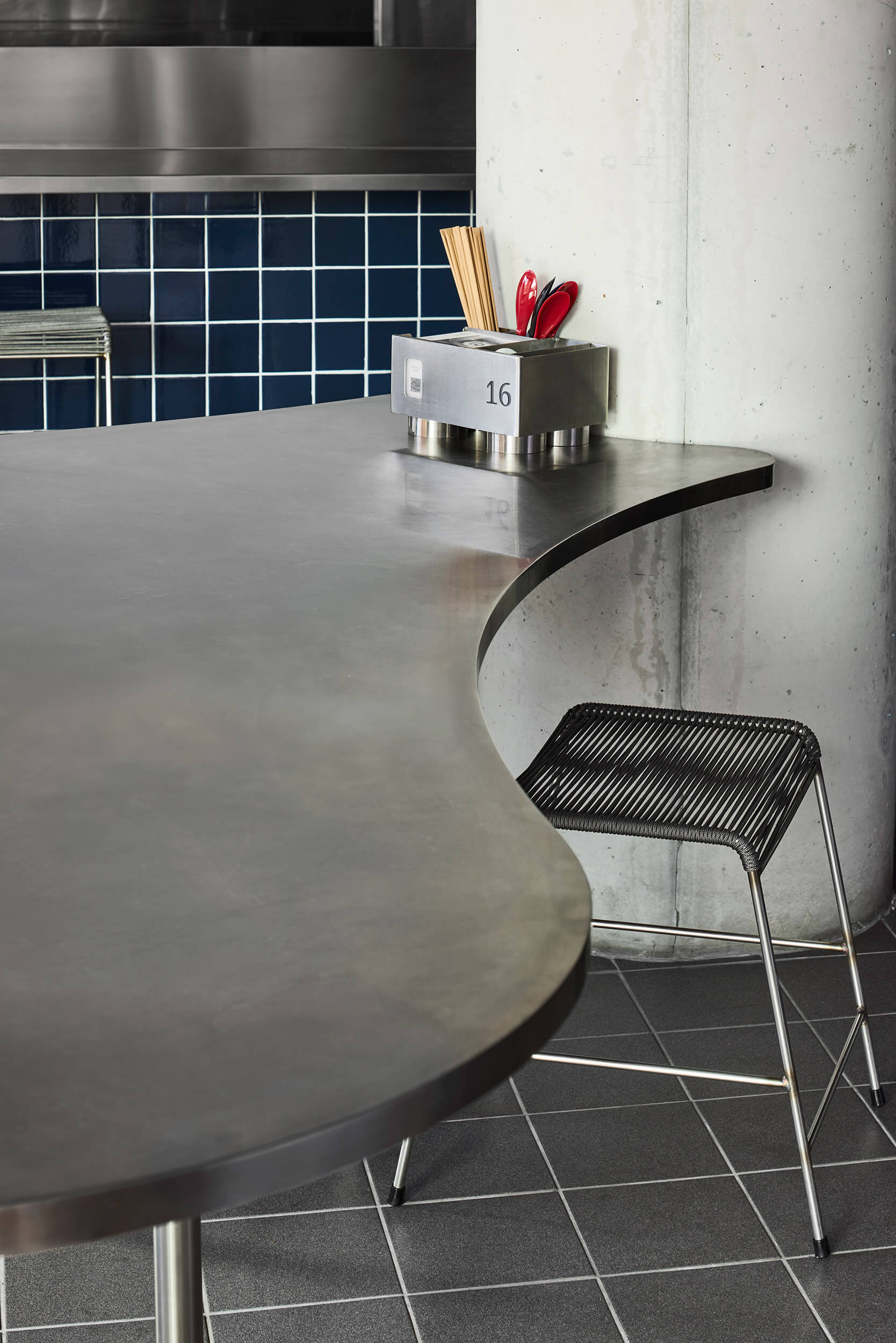 Curved metal countertop meeting concrete column with navy square tile backsplash