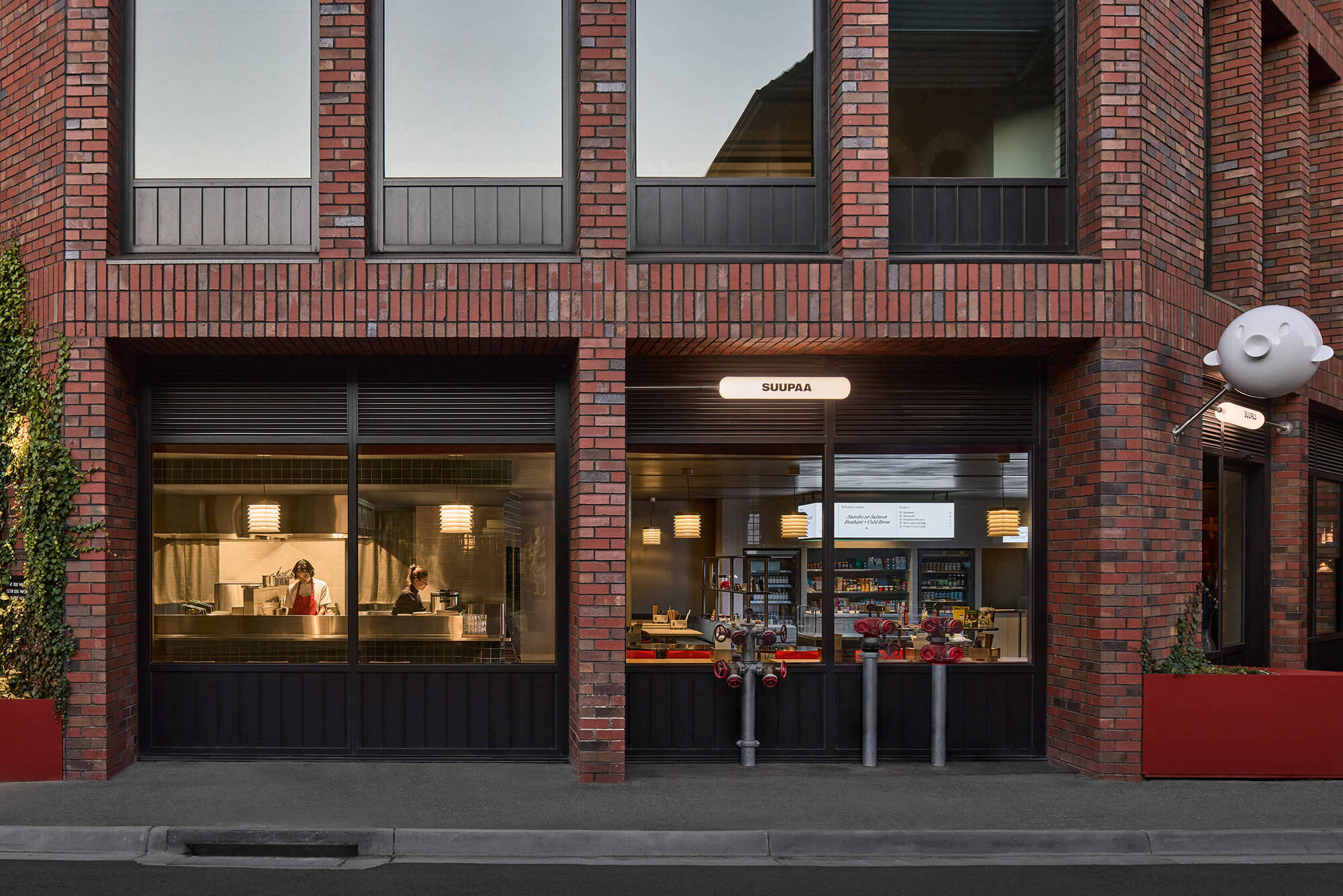 Street elevation showing dark brick facade with storefront glazing and residential balcony above at dusk