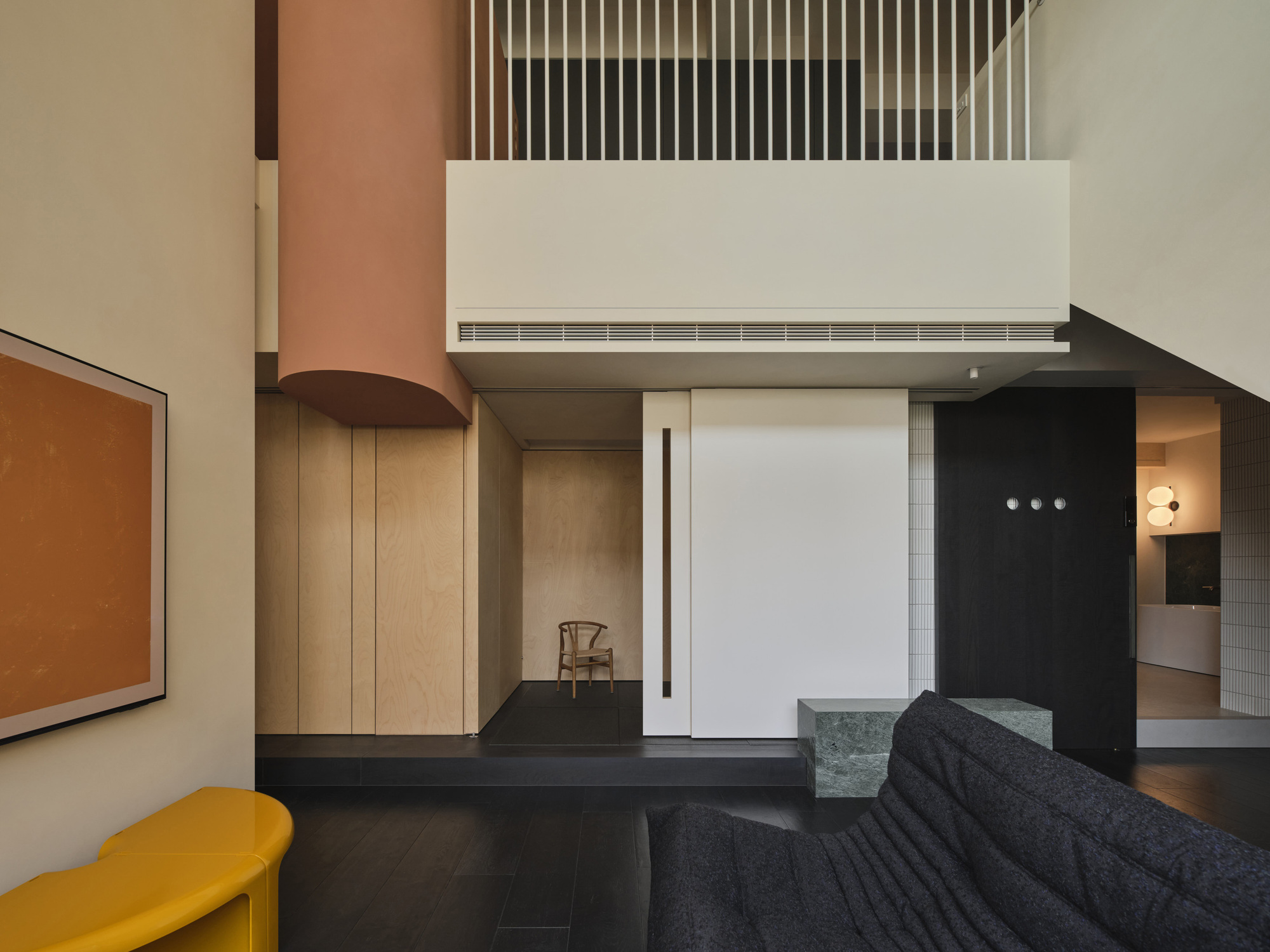 Double-height living space with vertical timber slat balustrade and suspended cylindrical terracotta duct in afternoon light