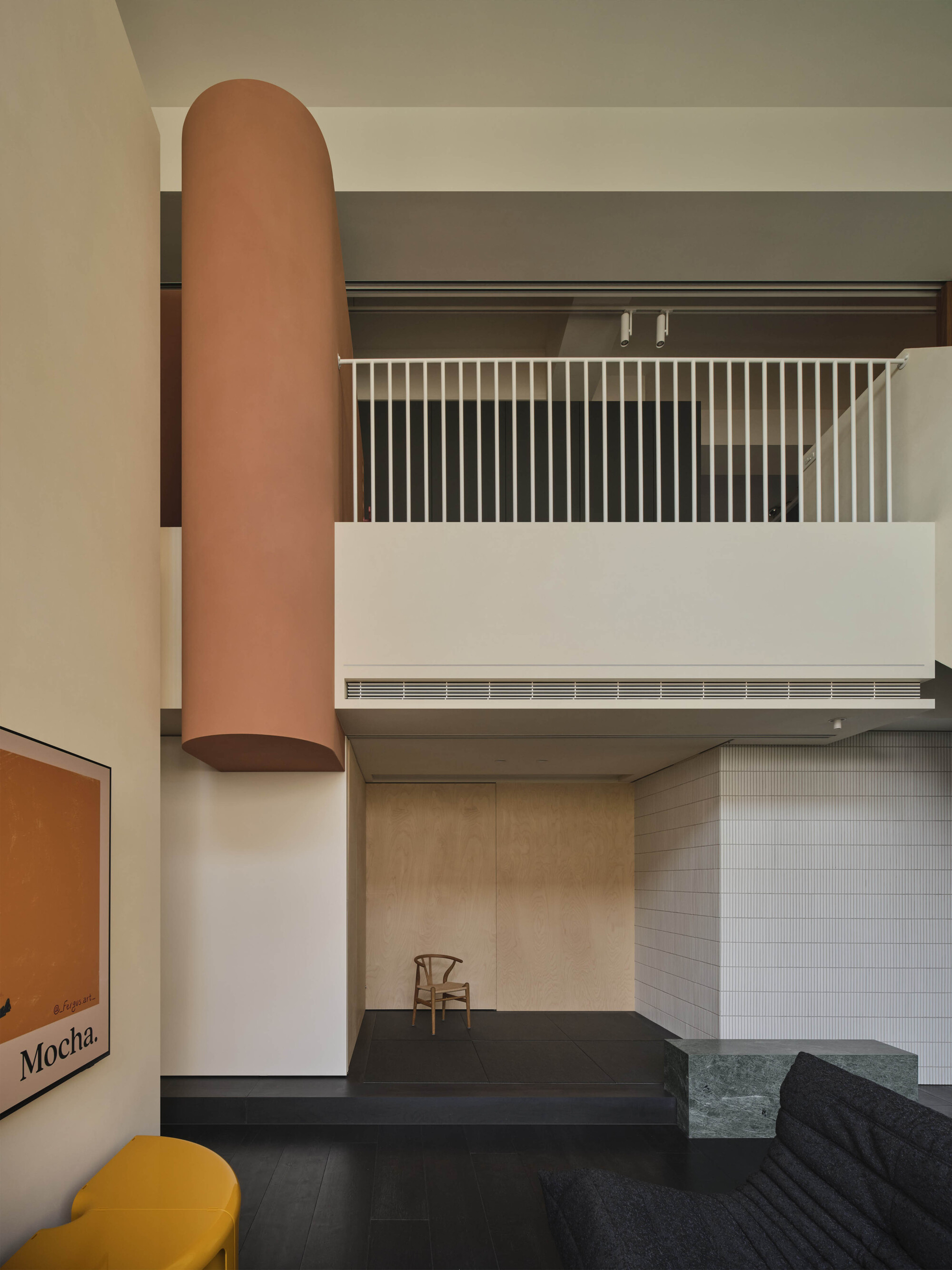 View of cylindrical terracotta column rising through the interior alongside white metal balustrade and wood paneled walls