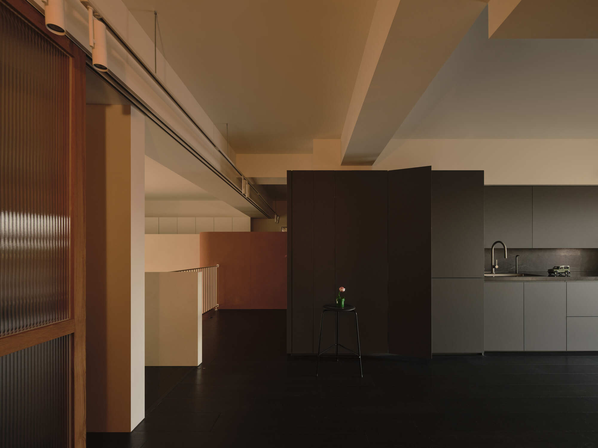 Ribbed glass sliding partition and freestanding black partition wall flanking kitchen with stepped ceiling beams above