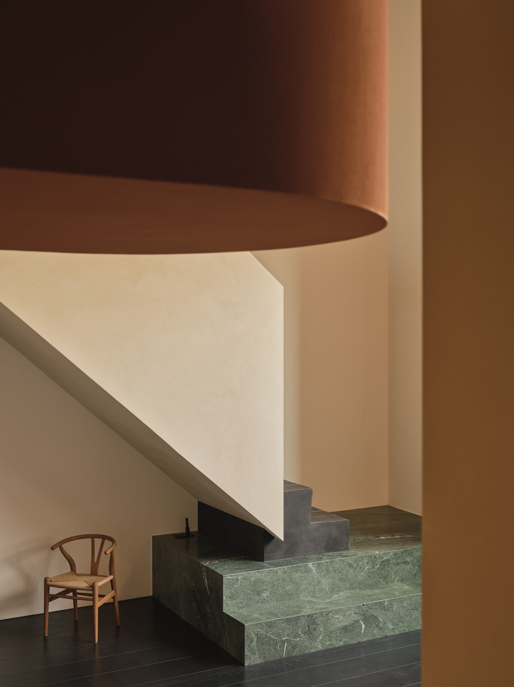 Close-up of green marble stair treads below curved white soffit and cylindrical terracotta column in warm light
