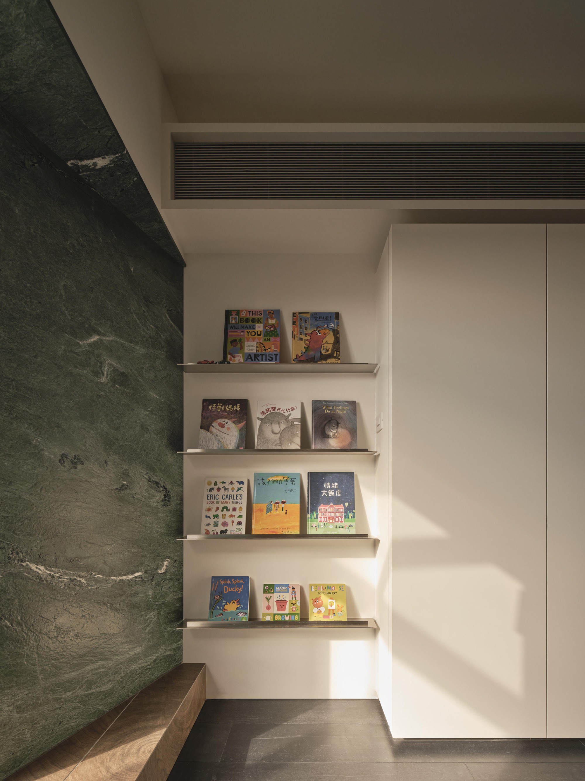 Corner nook with floating shelves displaying books beside a green marble wall