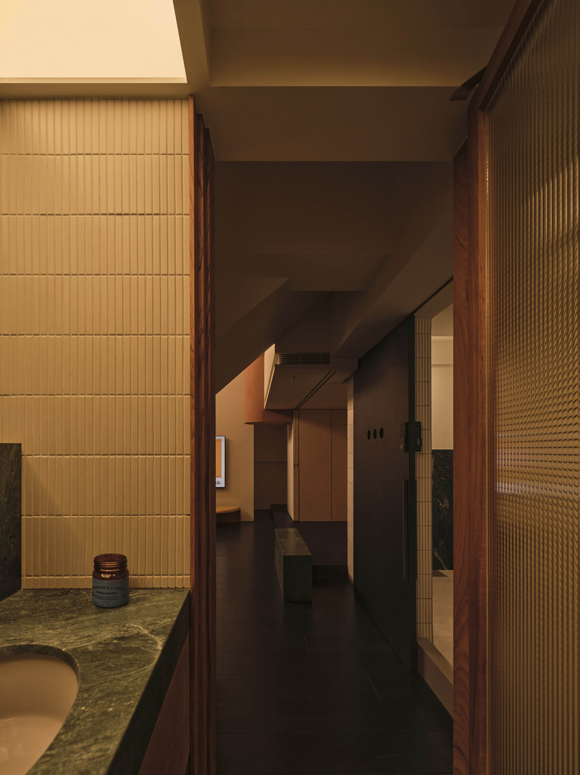 Corridor with ribbed glass panels and horizontal tile wall bathed in warm ambient light