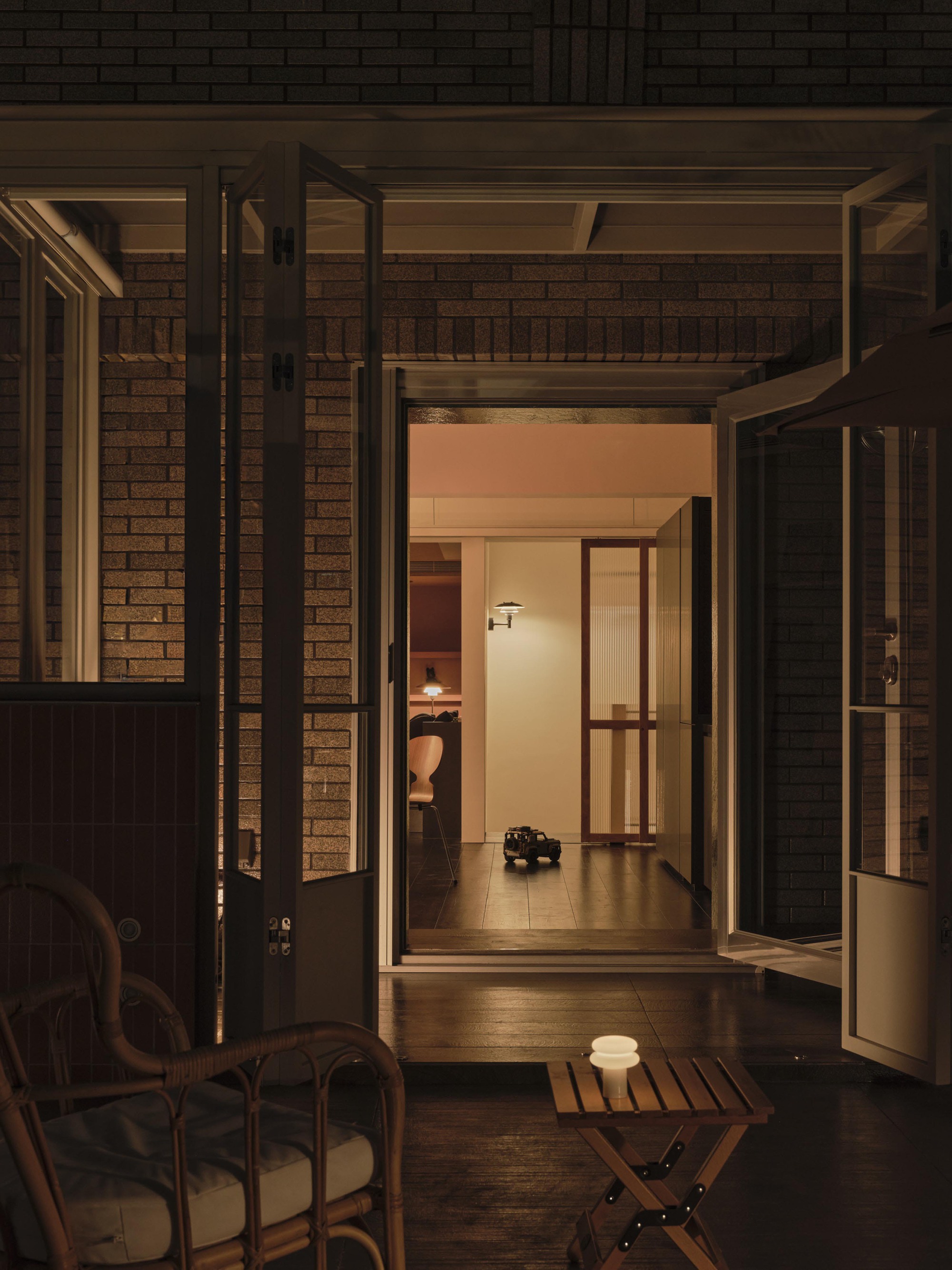 Open timber framed doors leading from dark brick courtyard into illuminated interior corridor at evening