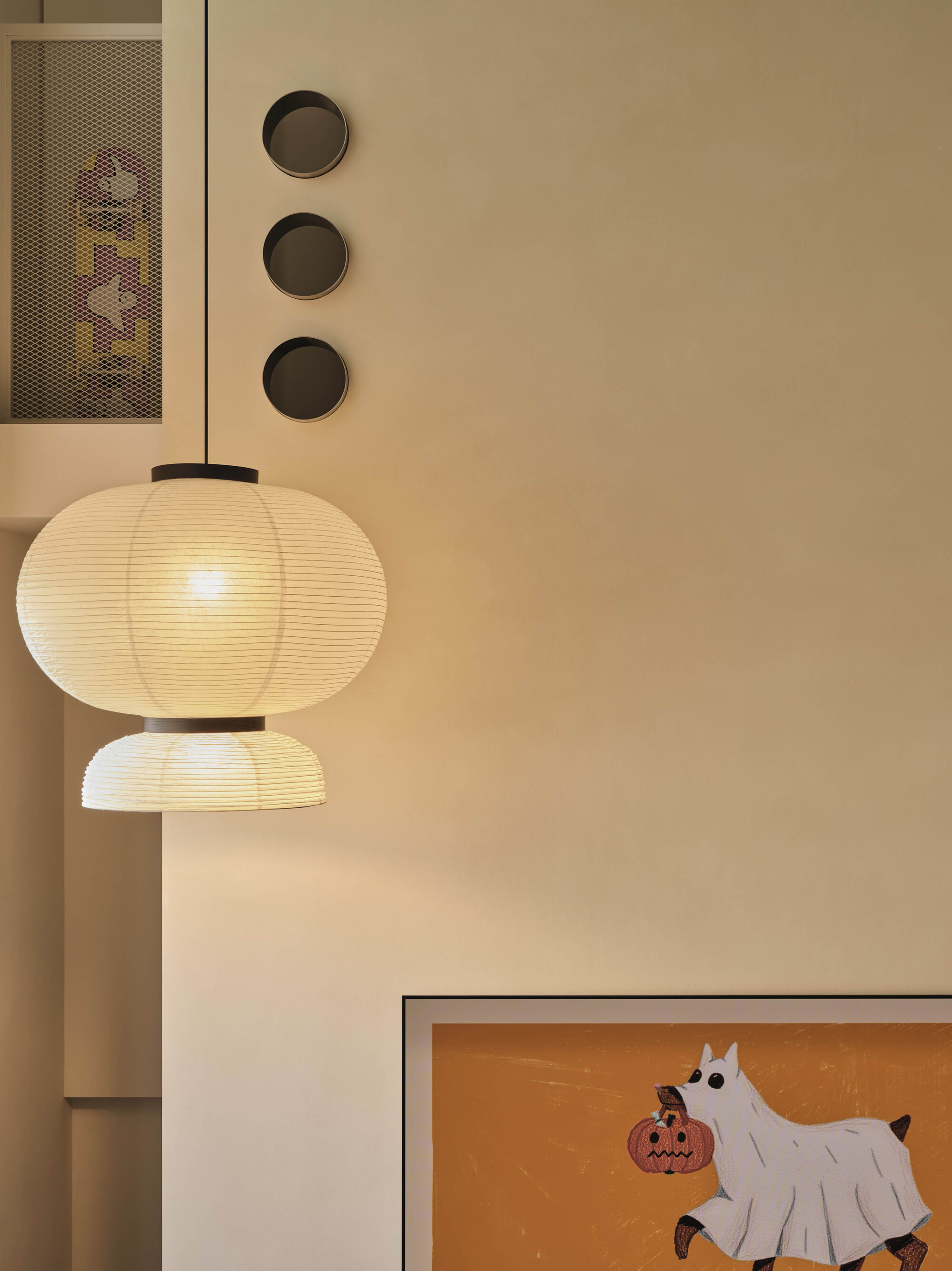 Paper lantern fixture beside a wall with three circular recesses and a framed drawing below