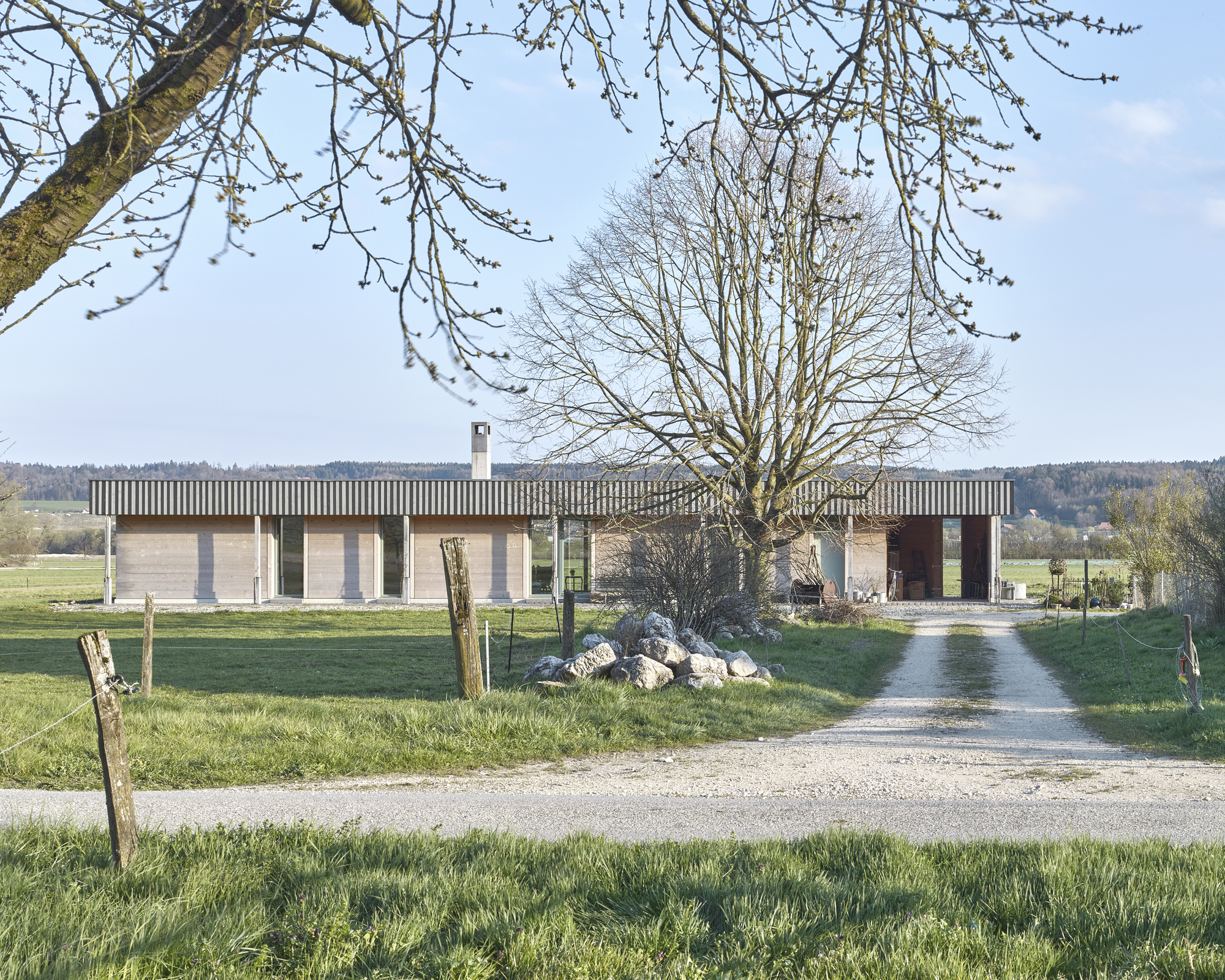 Linear single-story residence with vertical timber sunshades above concrete block walls framed by bare winter trees