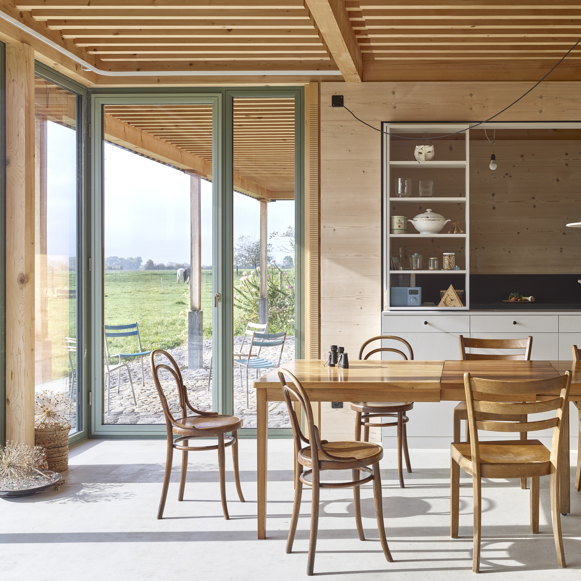 Dining area with timber ceiling beams and sliding glass doors opening to a covered terrace in daylight