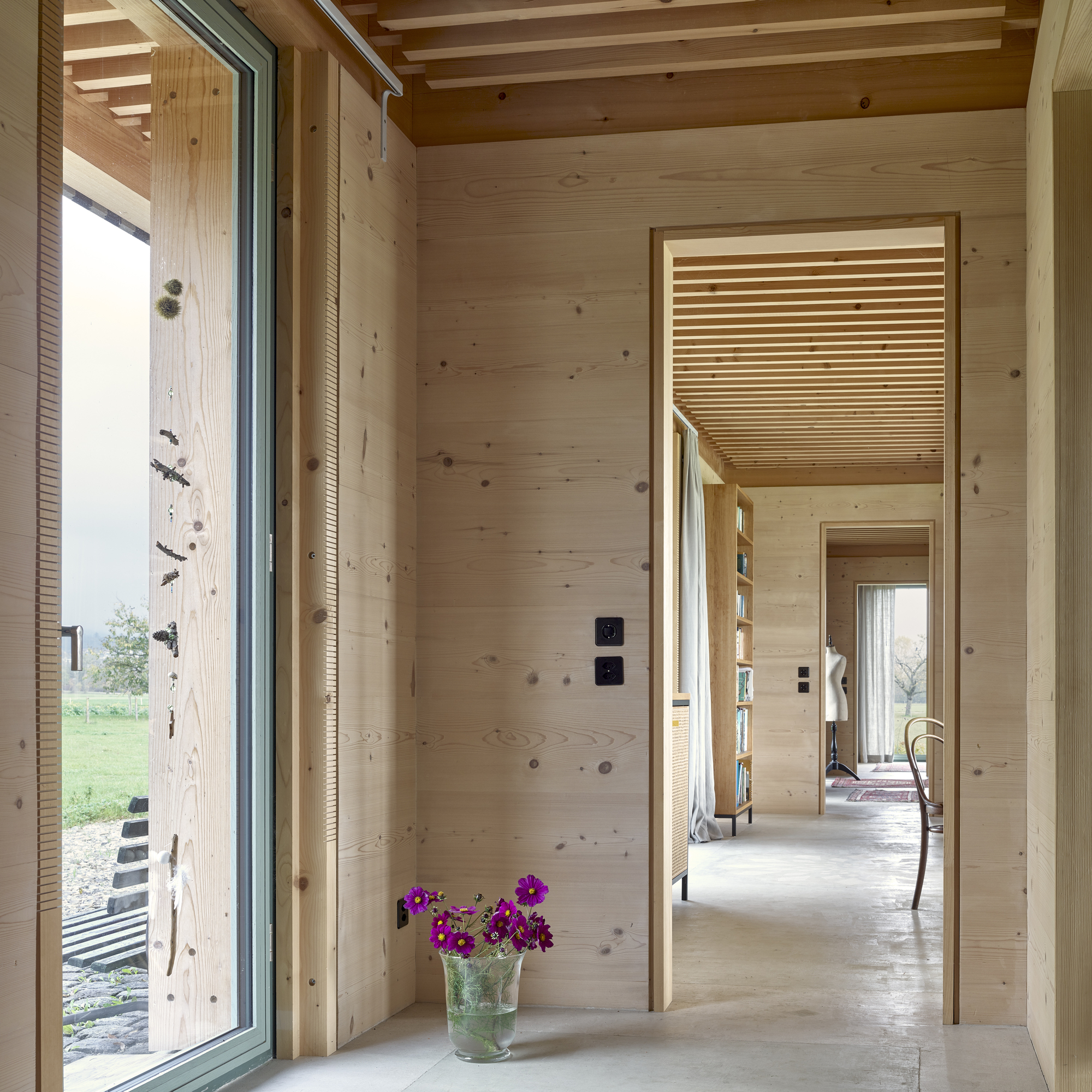 View through aligned doorways showing timber-clad walls, slatted ceiling inserts, and purple flowers on the floor