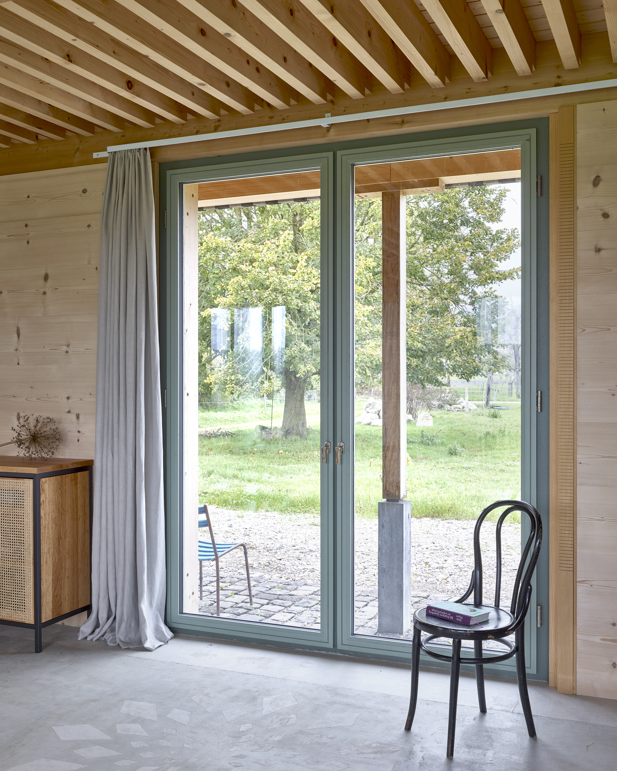 Glazed door opening to gravel terrace with a bentwood chair beneath an exposed timber beam ceiling