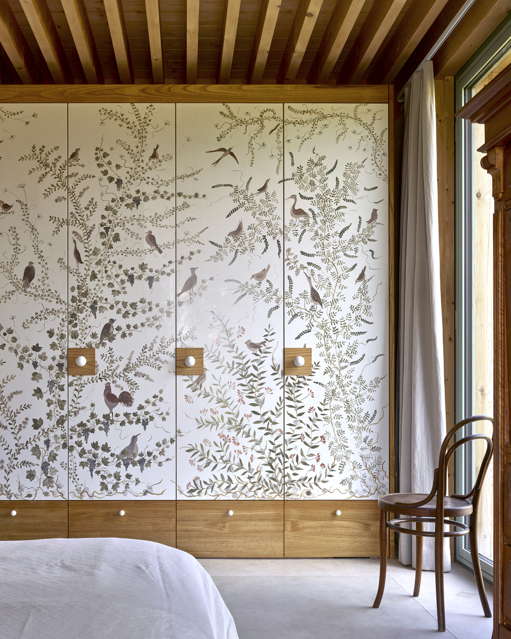 Built-in wardrobe with hand-painted bird and botanical panels flanked by timber drawers in a bedroom
