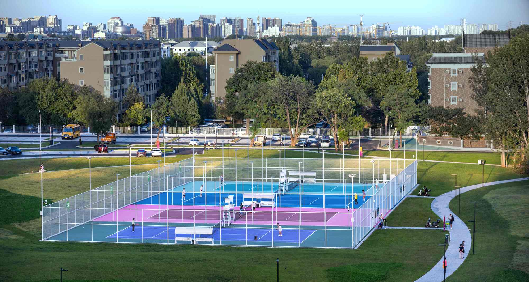 Multi-colored courts enclosed by white mesh fencing with residential buildings visible in the background
