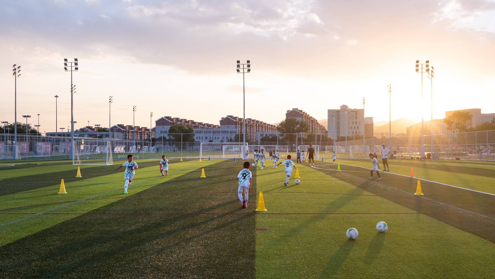 Youth soccer practice on artificial turf fields with yellow training cones at golden hour