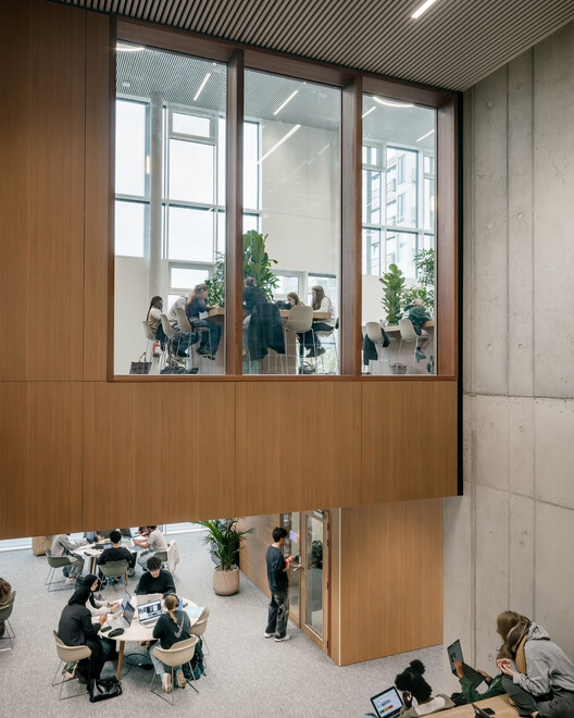 Reading room with double-height void: oak-panelled meeting rooms looking onto the atrium below, exposed concrete columns and soffit, group work tables