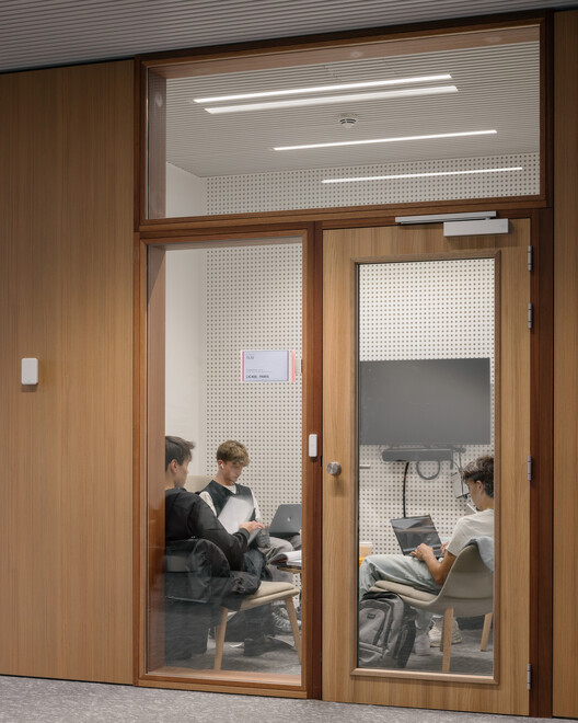 Group study room: timber door and frame, perforated acoustic panel, two students working inside at a timber table with laptops