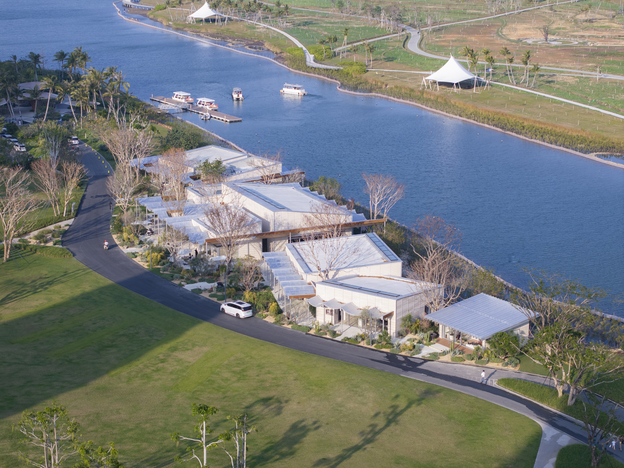 Aerial view of white flat-roofed volumes clustered along a canal with boats and palm trees