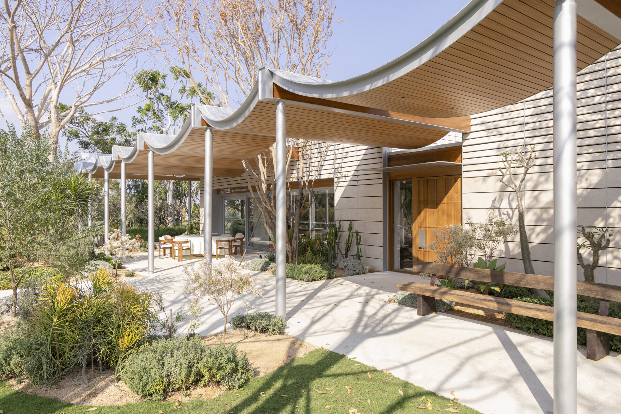Covered terrace with undulating wood ceiling and white columns framing a landscaped courtyard with bare trees