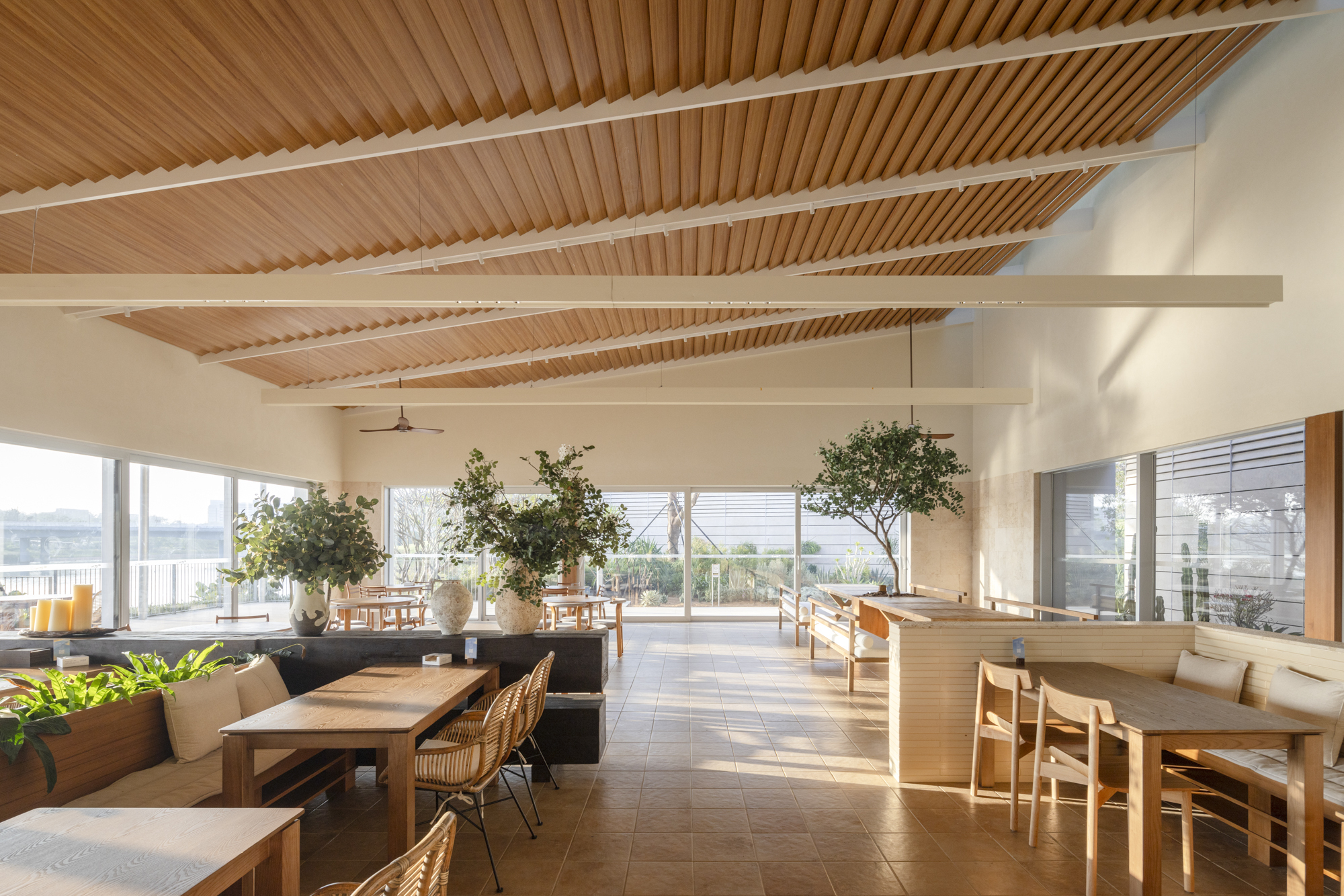 Open dining area with slatted wood ceiling beams and potted trees in afternoon sunlight