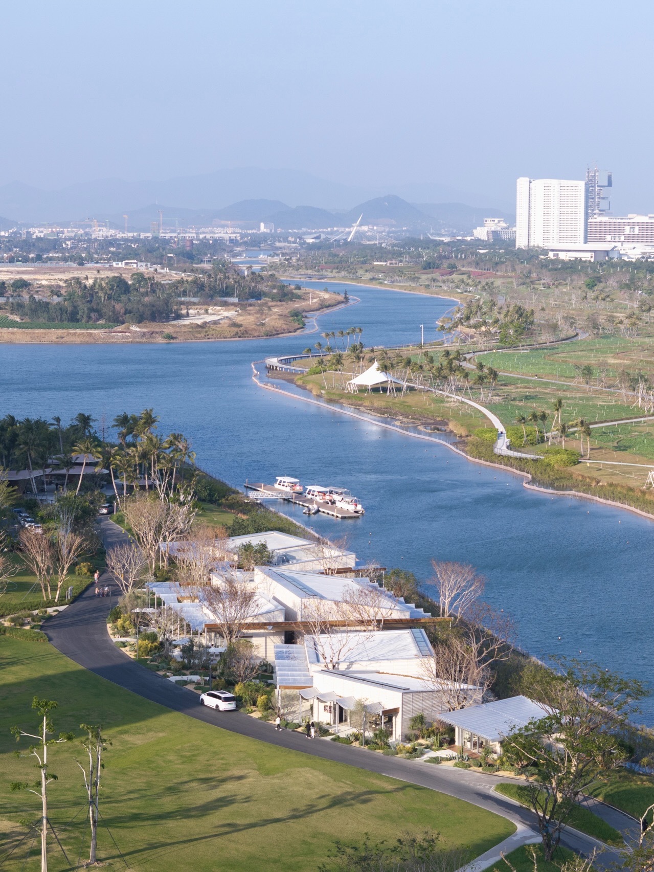 Aerial view of white undulating rooflines along a meandering riverbank with scattered palms and lawn