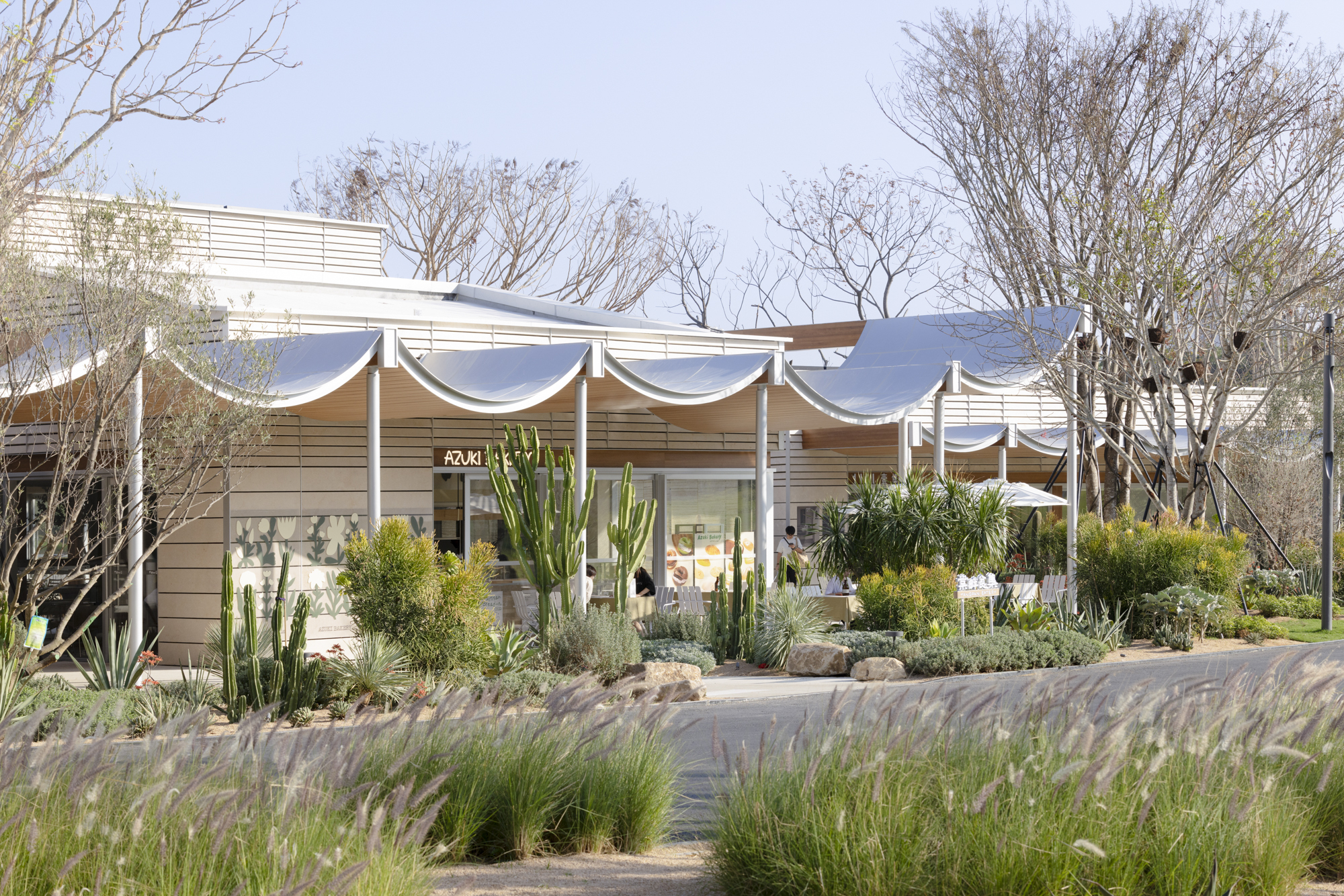 Fabric canopy with white columns shading a glazed pavilion surrounded by cacti and desert grasses
