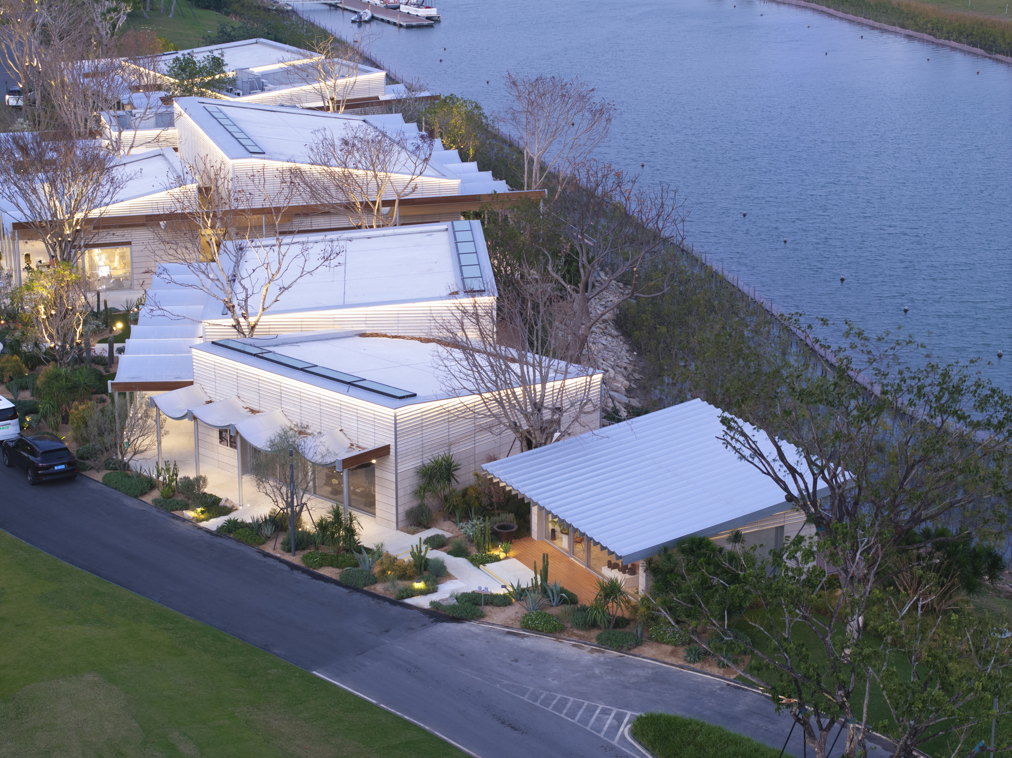 Aerial view of corrugated metal roofs cascading down a planted slope toward the water at dusk