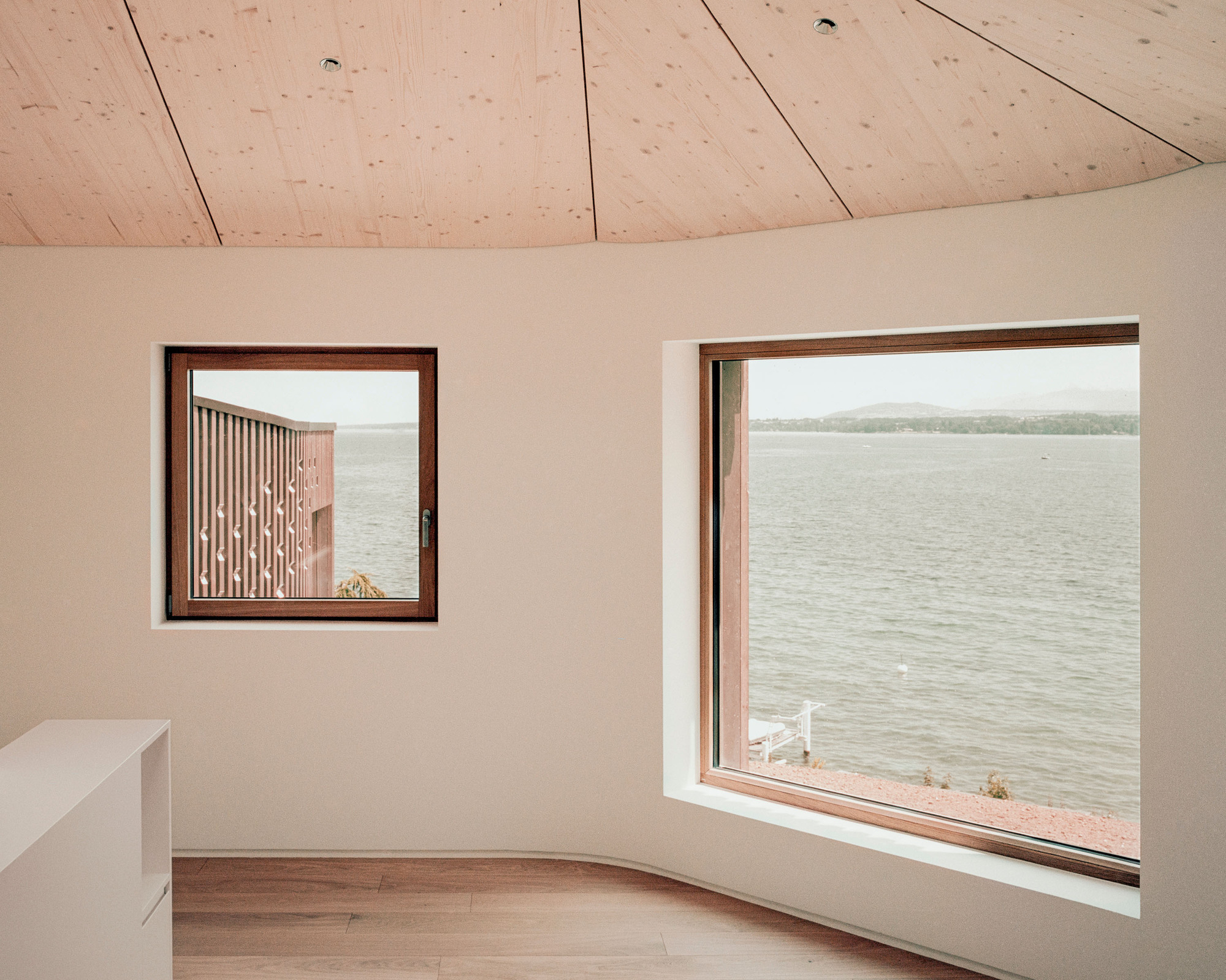 Interior room with plywood vaulted ceiling and two windows framing views of the water