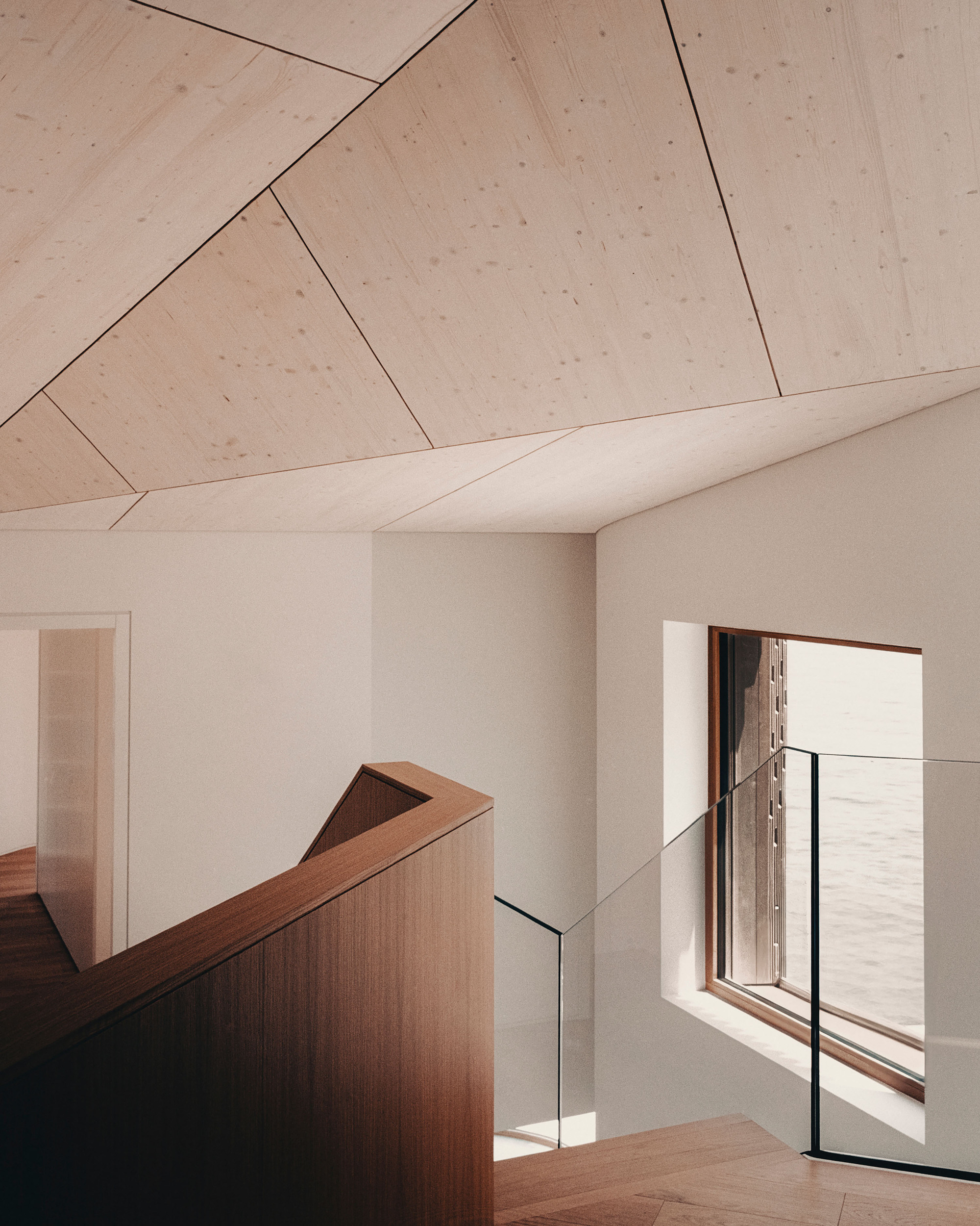 Stairwell with timber handrail and glass balustrade under a faceted plywood ceiling