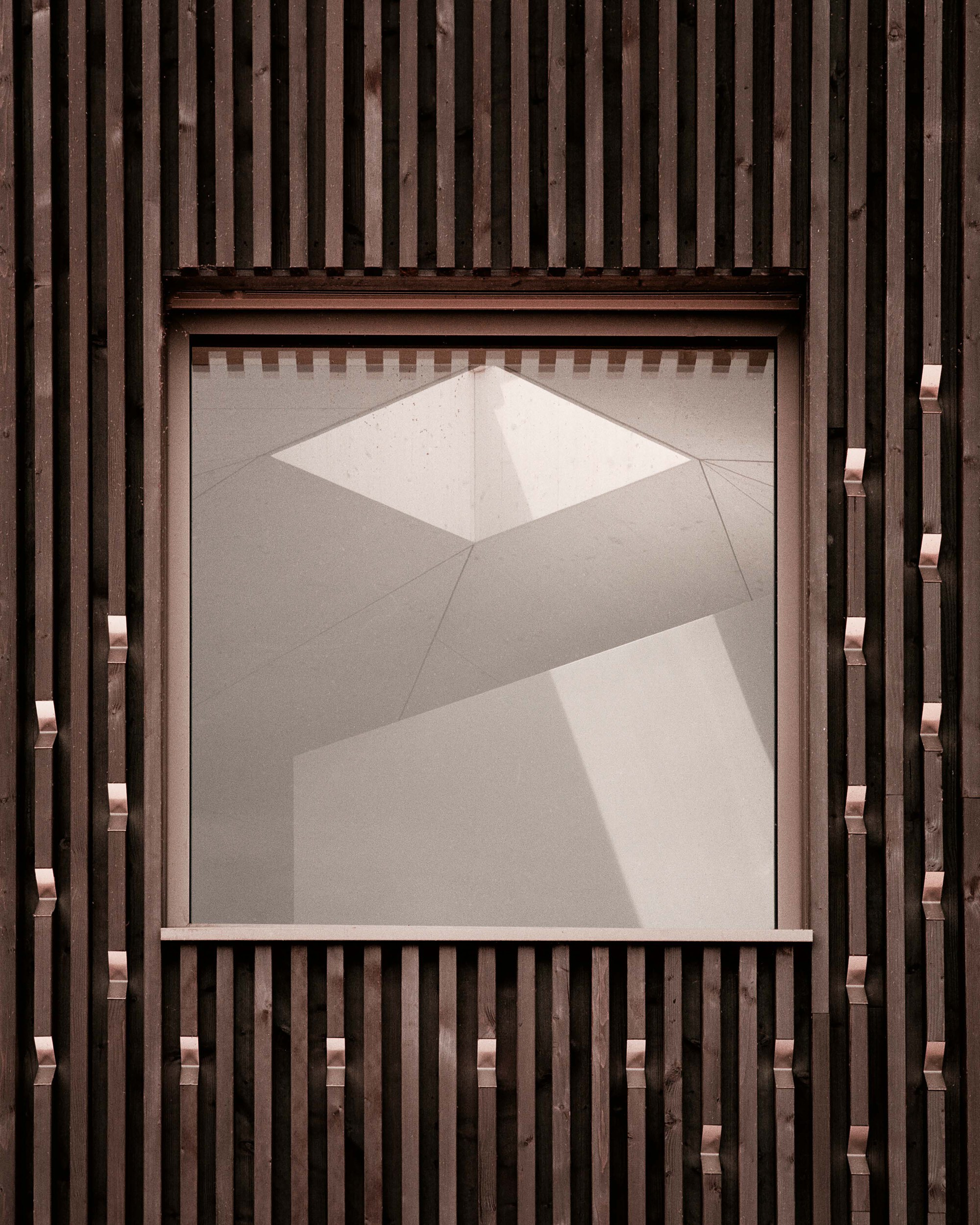 Recessed window framed by vertical timber slats with angular shadow patterns on the ceiling
