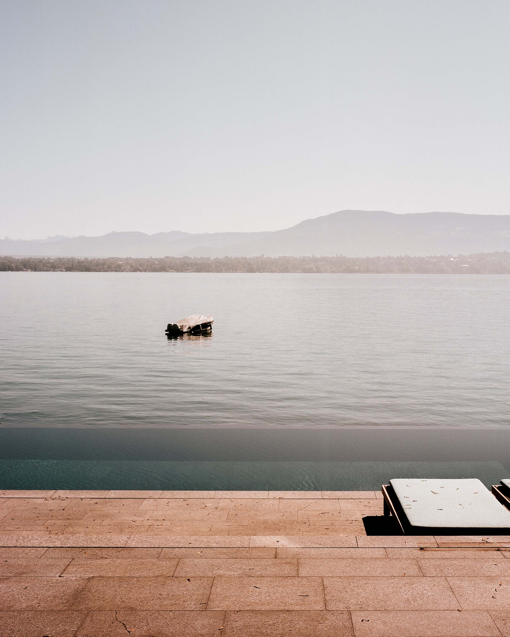Terracotta tile terrace with infinity pool edge and sunbed facing distant mountains across the water
