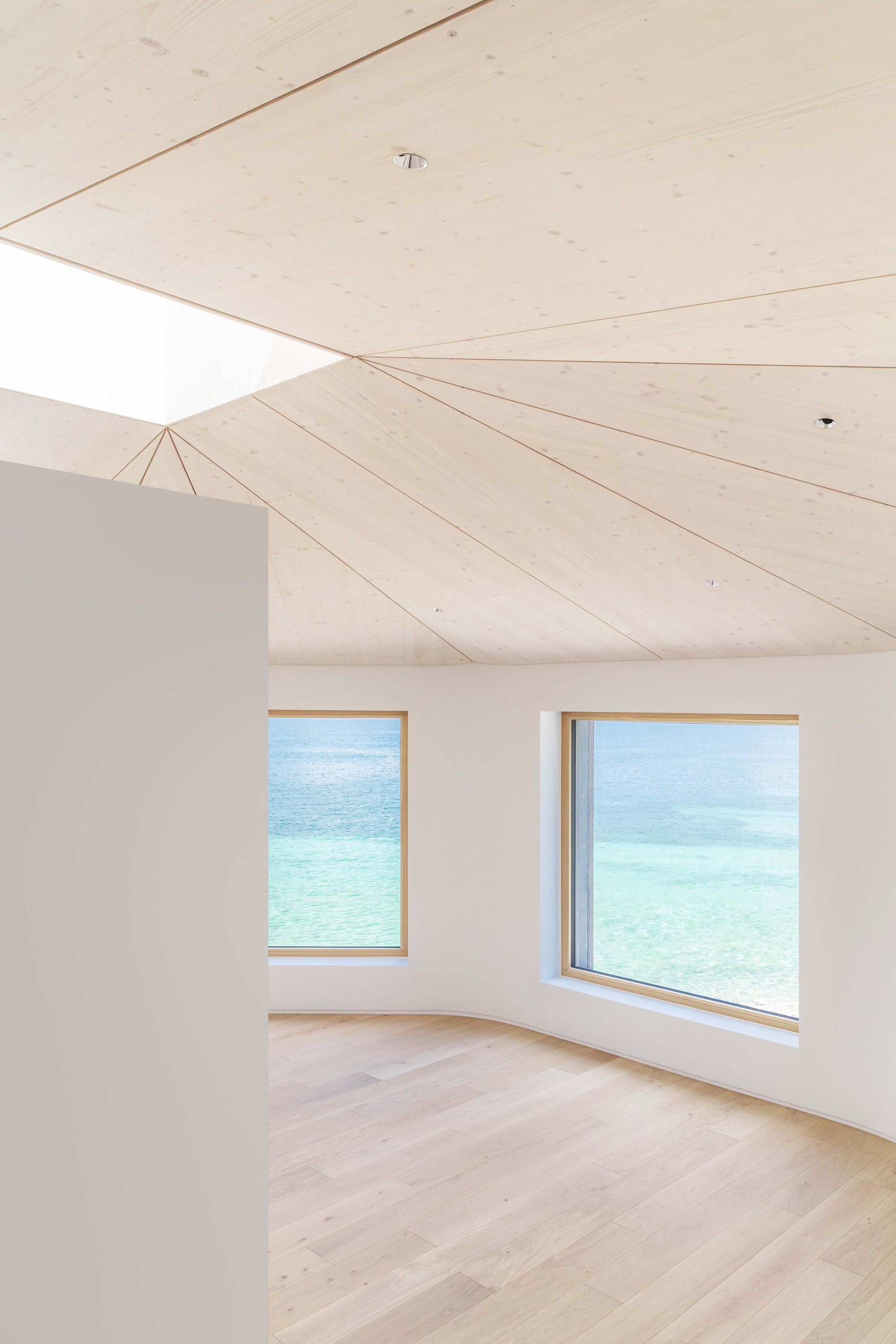 Interior room with pale timber plank ceiling and two timber-framed windows framing turquoise lake views