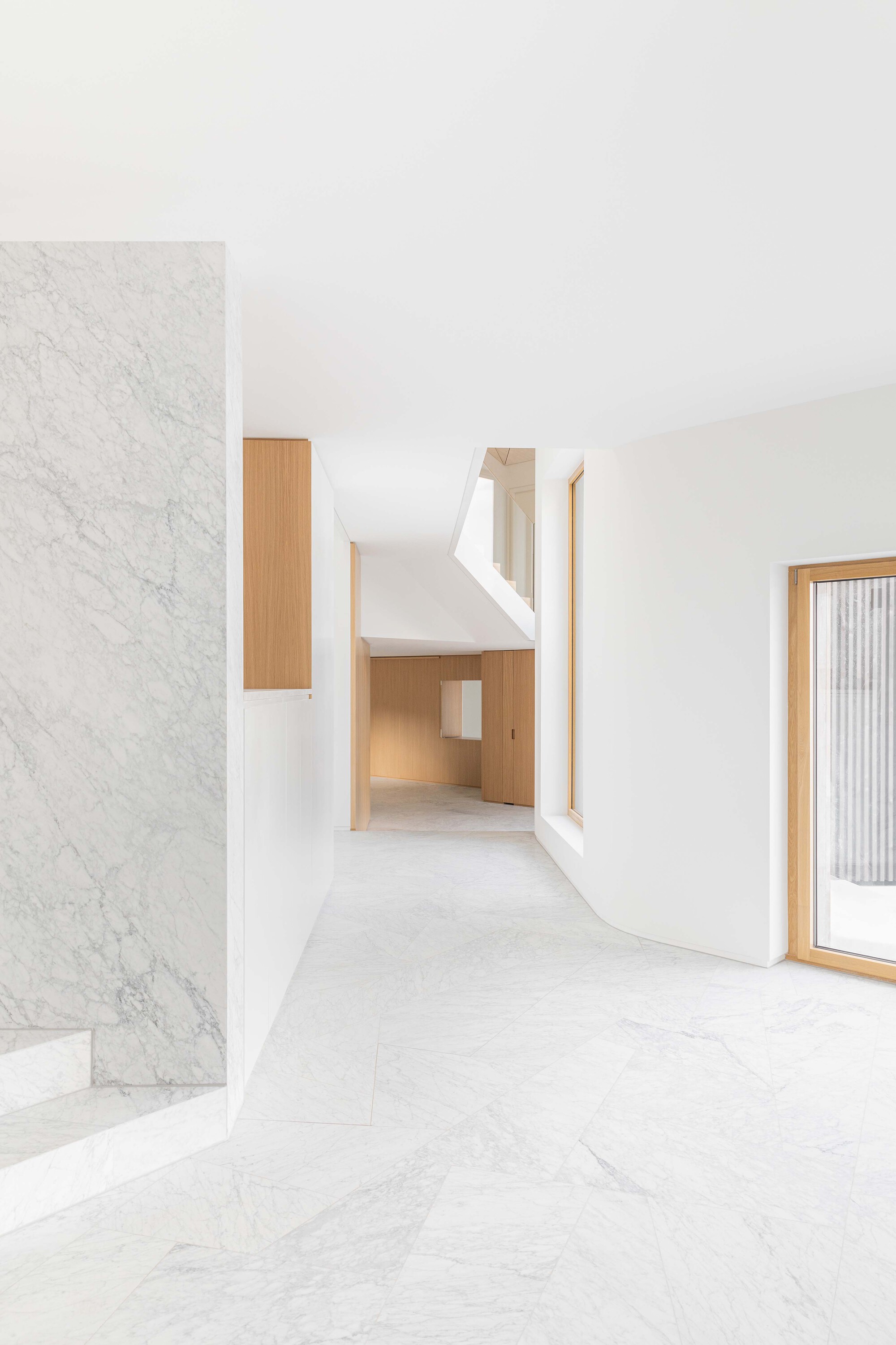 White marble stair beside timber cabinet opening into double height space with angled skylight above