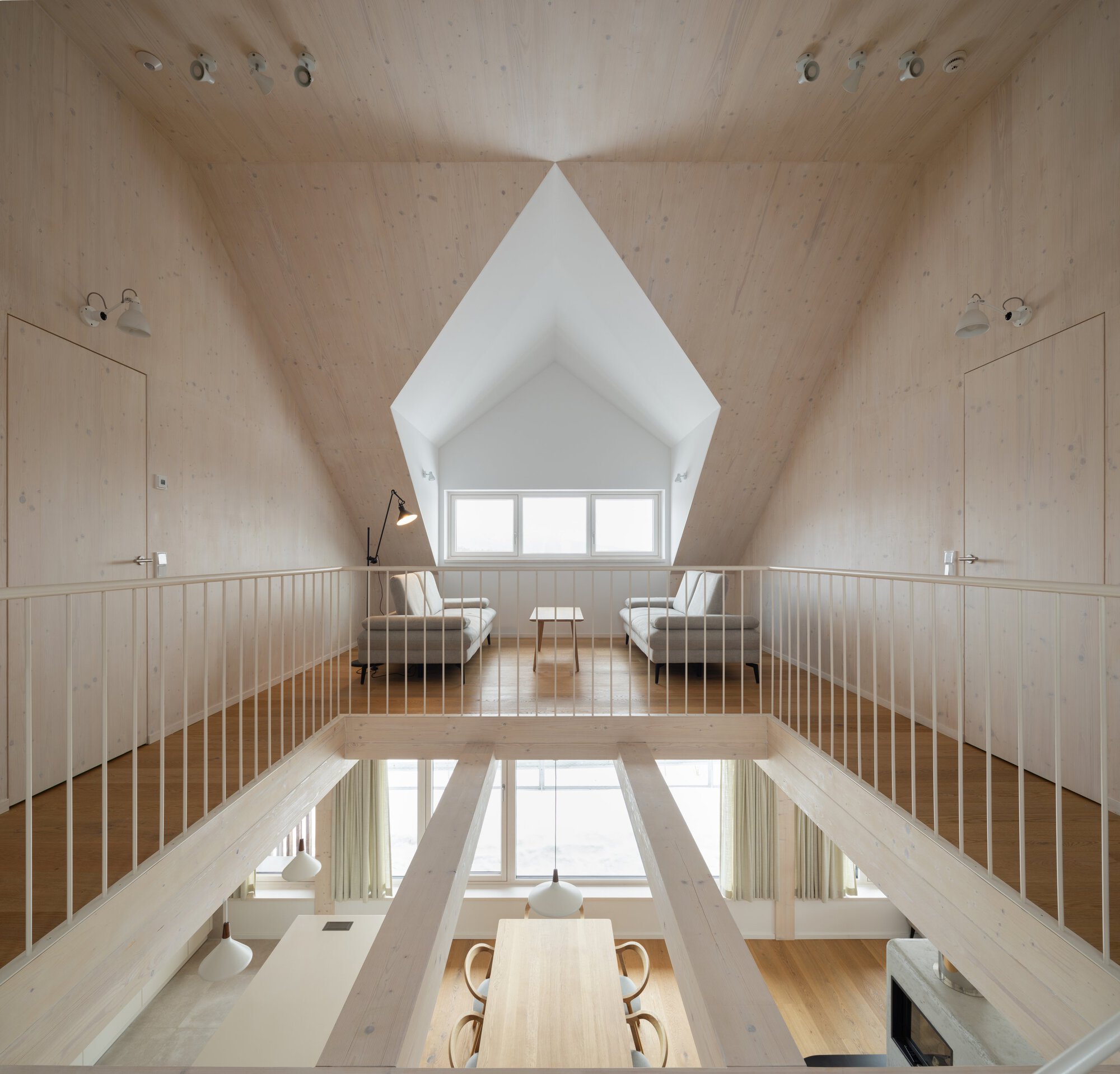 Mezzanine reading nook overlooking dining area through timber slat railings under sloped plywood ceiling