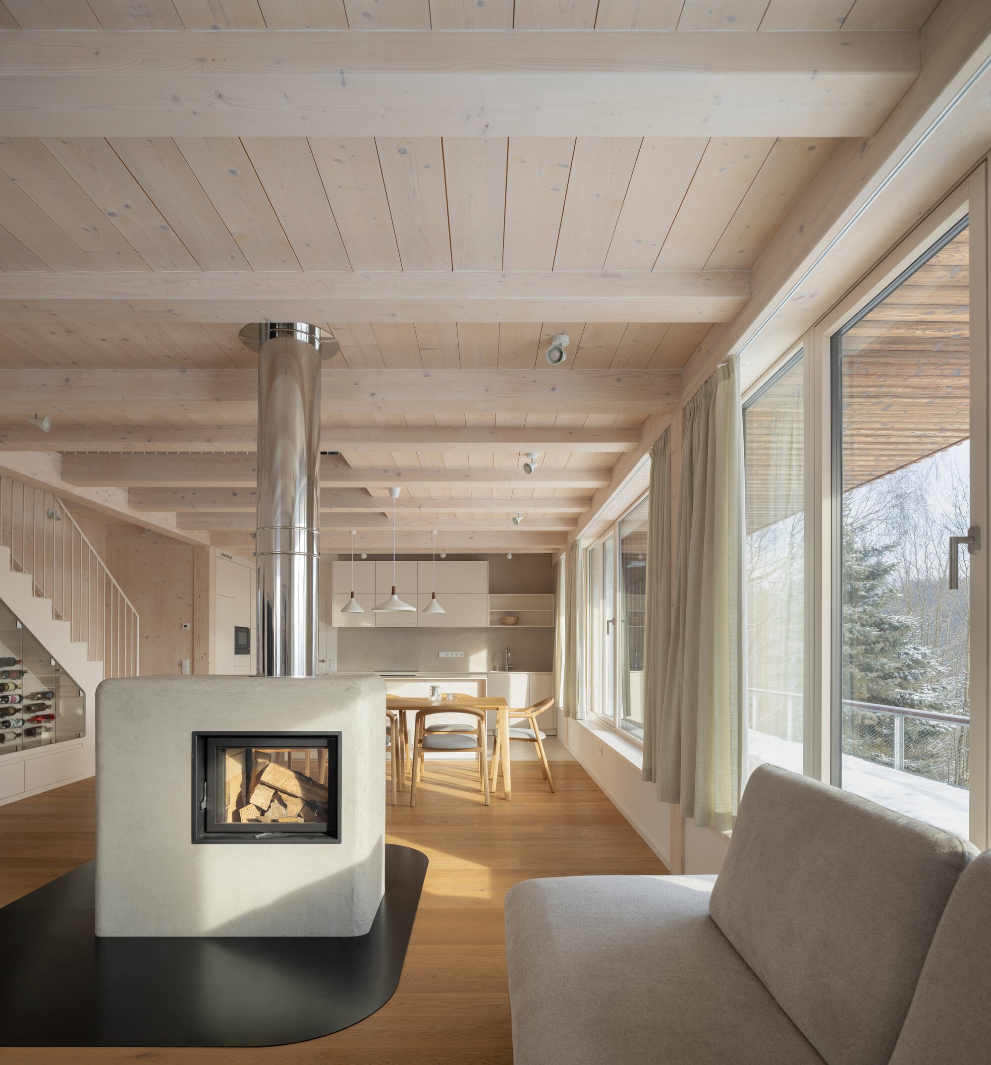 Open living space with exposed timber beam ceiling, central fireplace with steel flue, and view to snowy landscape