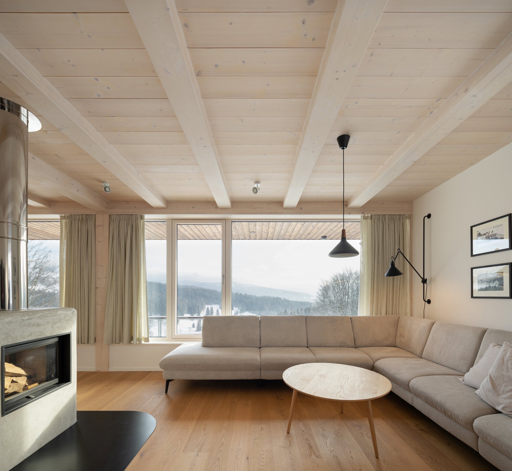 Living room with exposed timber ceiling beams, corner window wall framing winter mountain views, and pendant lighting