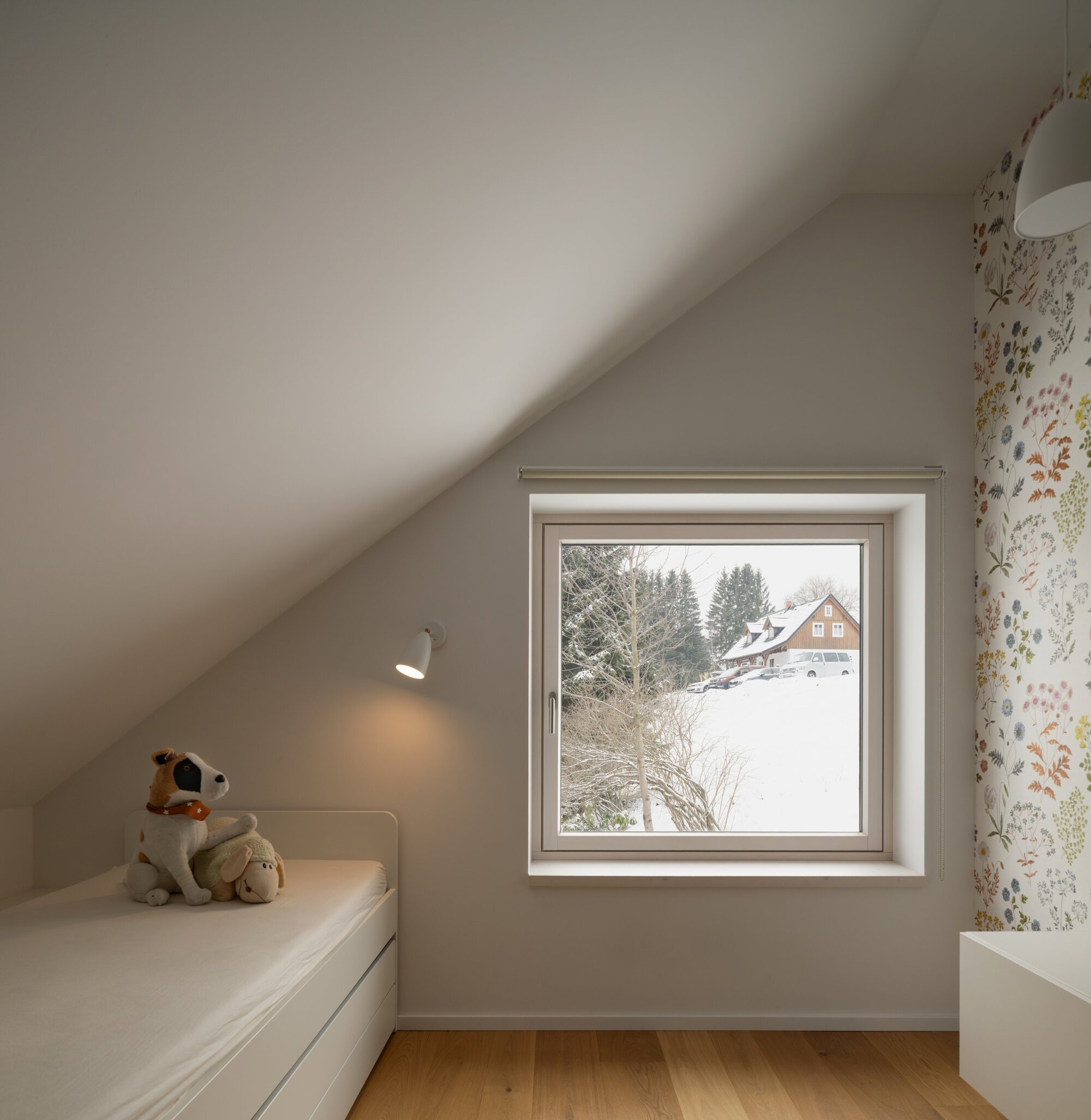 Bedroom window framing a snow-covered landscape with a neighboring timber house visible through the trees