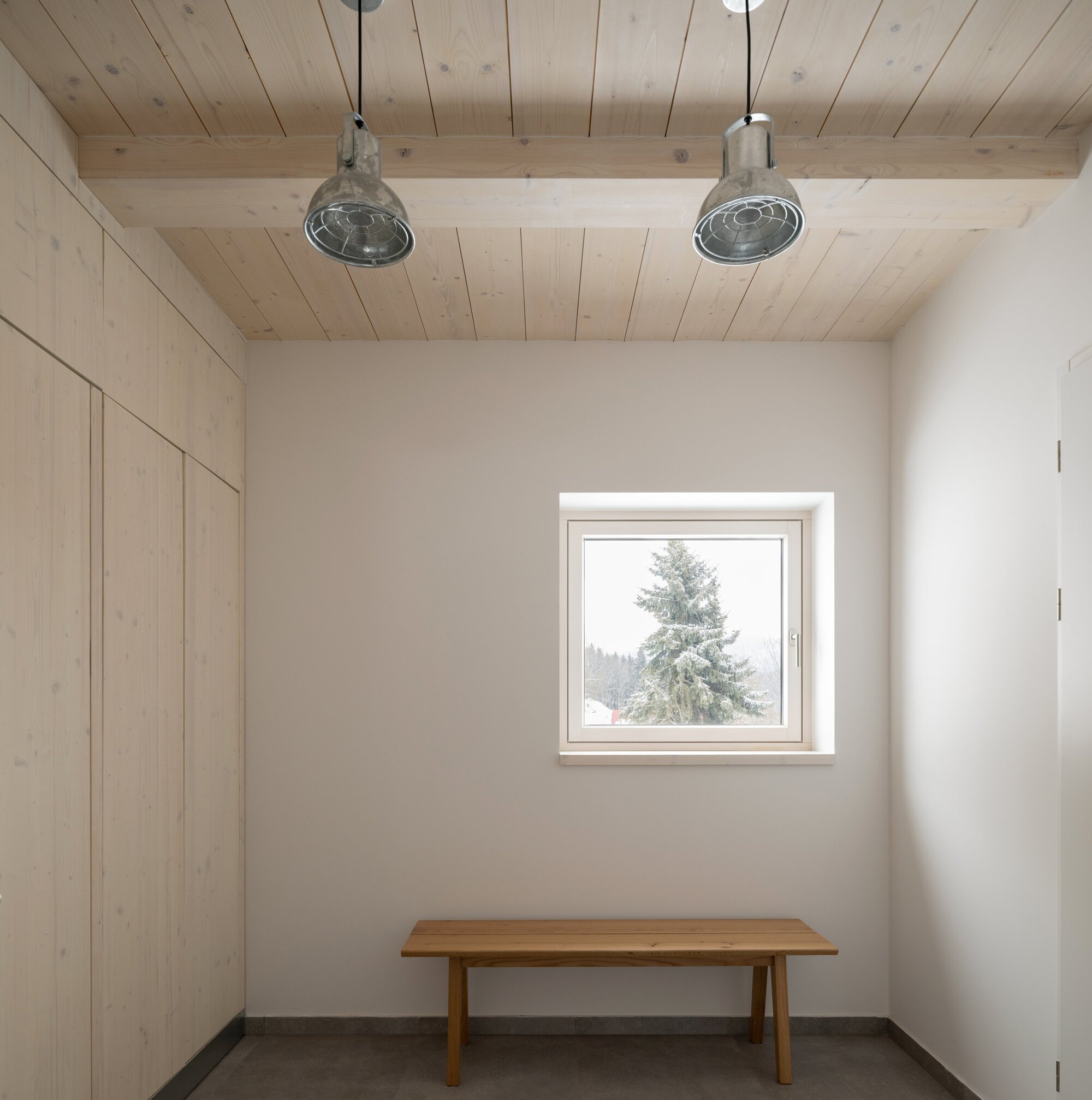 Entry space with timber bench beneath a square window looking out to a snow-dusted fir tree