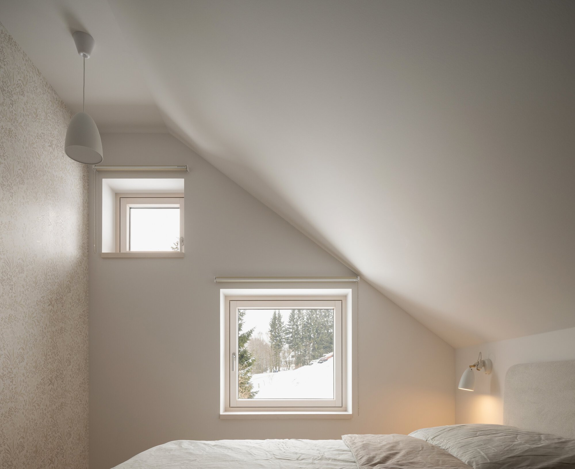 Bedroom with two staggered windows under a sloped ceiling revealing snowy forest views outside