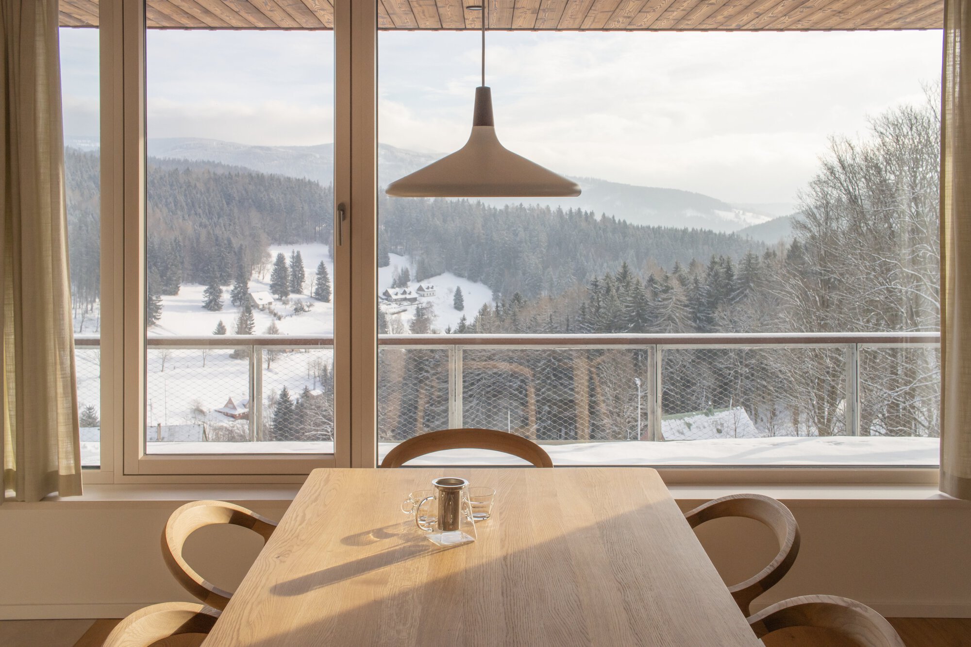 Dining table with pendant light overlooking wire mesh balcony railing and forested valley in winter