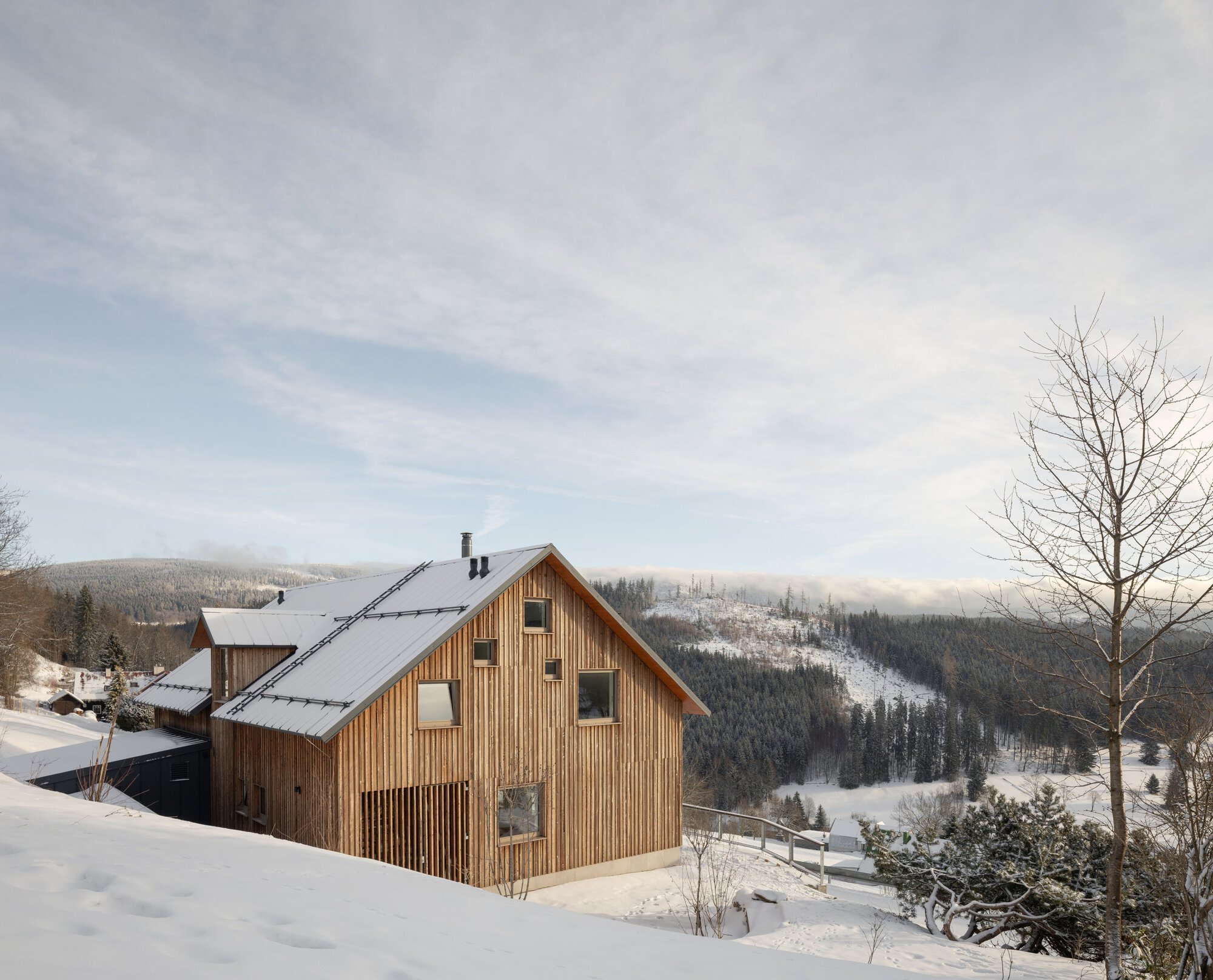 Pitched roof timber house overlooking a snow-covered valley with forested hills