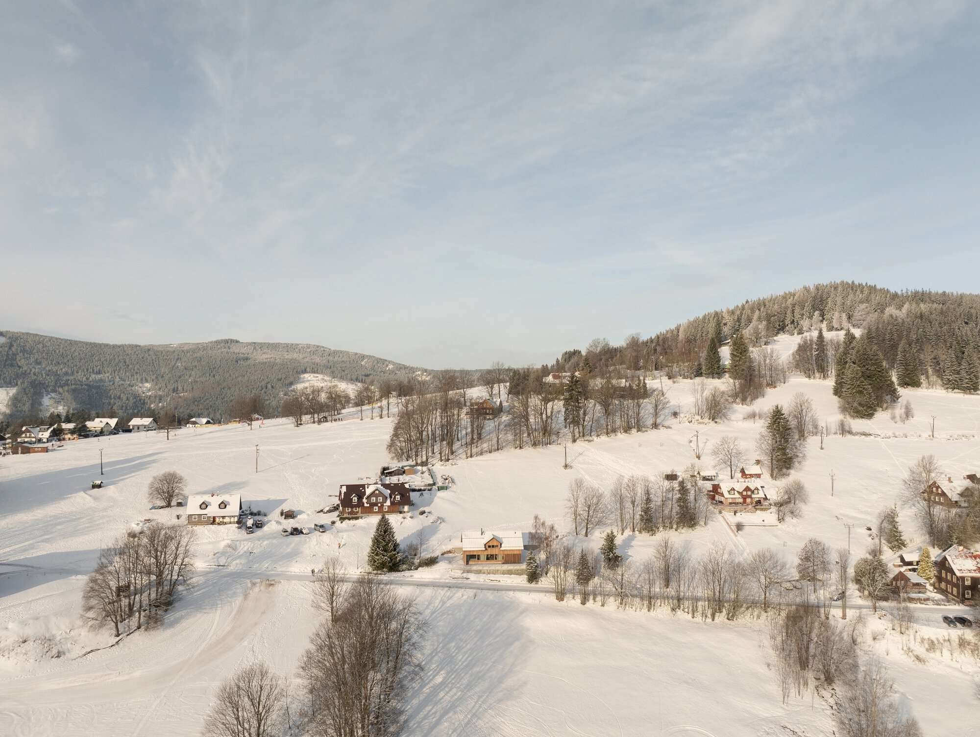 Aerial view of scattered houses across a snow-covered valley with wooded slopes